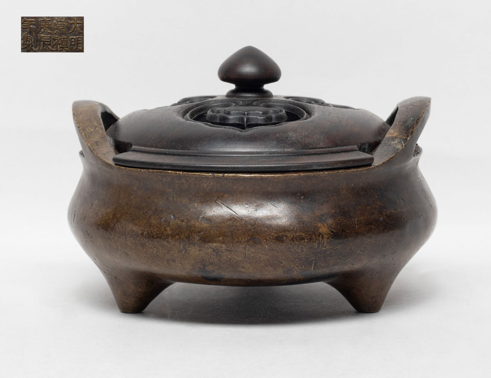 Estate Chinese Bronze Cabinet Censer w/ Cover: Of compressed form with two handles and three short tapered feet, the bottom inscribed with an eight-character mark, with a wood lid reticulated with three ruyi heads. Approx. 5.2*2.8 inch (w/o lid).