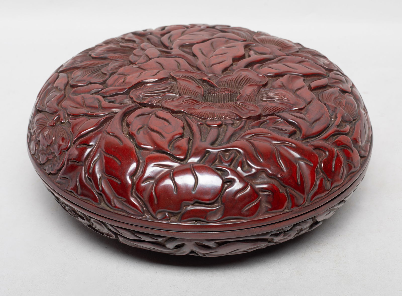 Chinese Cinnabar Like Covered Box: Of circular shape, carved around the exterior with large blooms issuing from overlapping leafy stems. Approx. 7*2.5 inch.