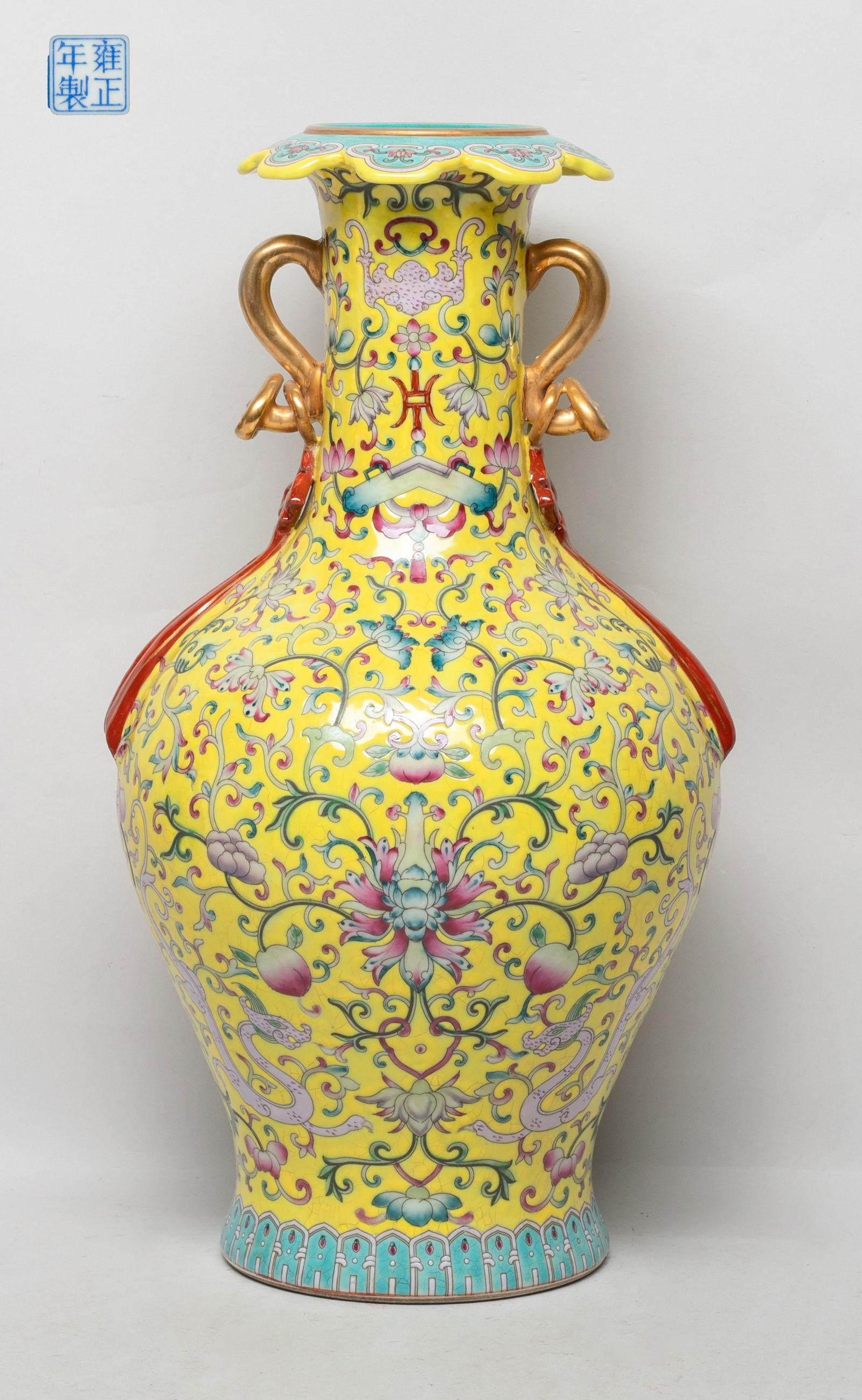 Tall Chinese Famille Rose Porcelain Vase: The vase exterior enameled with dense foliage stems issuing lotus and peaches, interspersed with dragons, bars and traditional instruments, against bright yellow ground, flanked by two handles in form