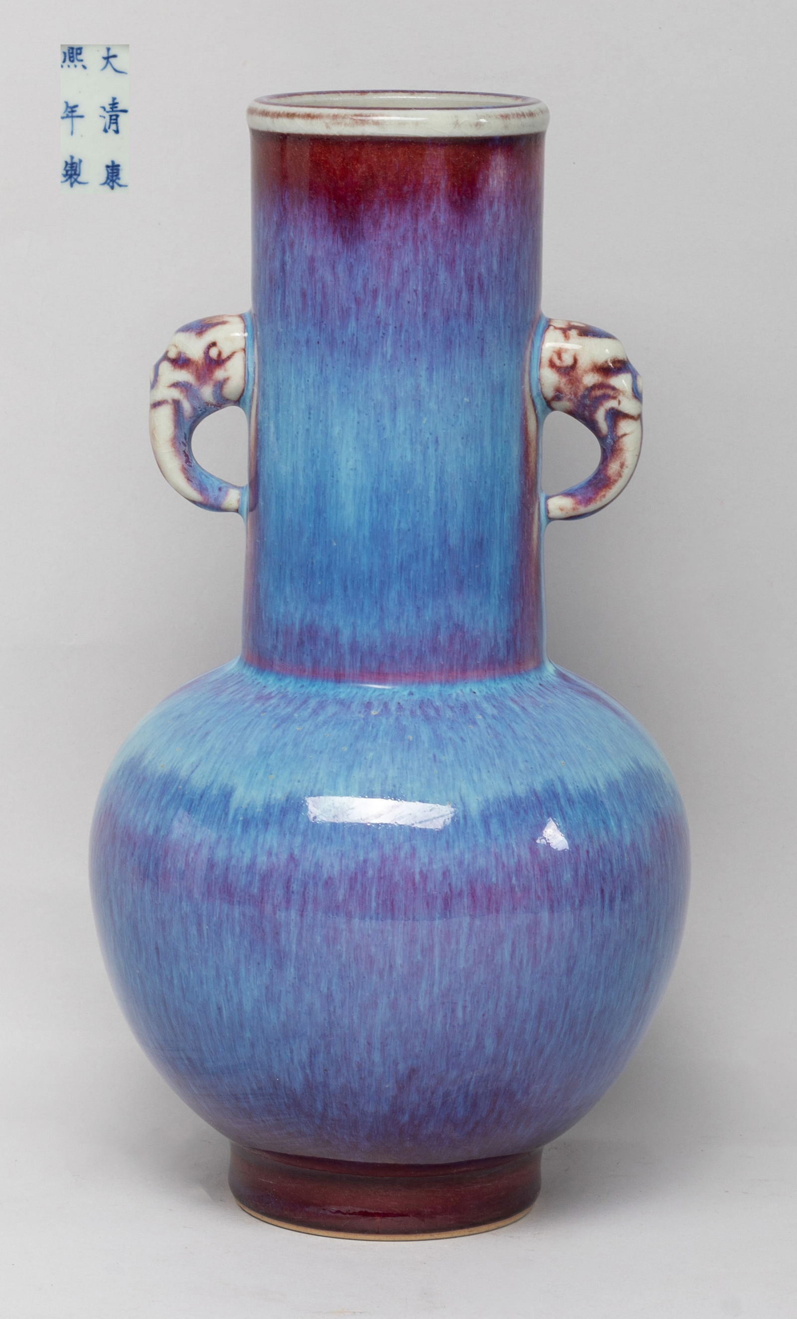 Chinese Flambe Glazed Porcelain Vase: The globular body rising from a short foot to a tall columnar neck, flanked by two handles issuing from beast heads, covered in rich purple-red glaze suffused with lavender blue streaks, the bottom ma