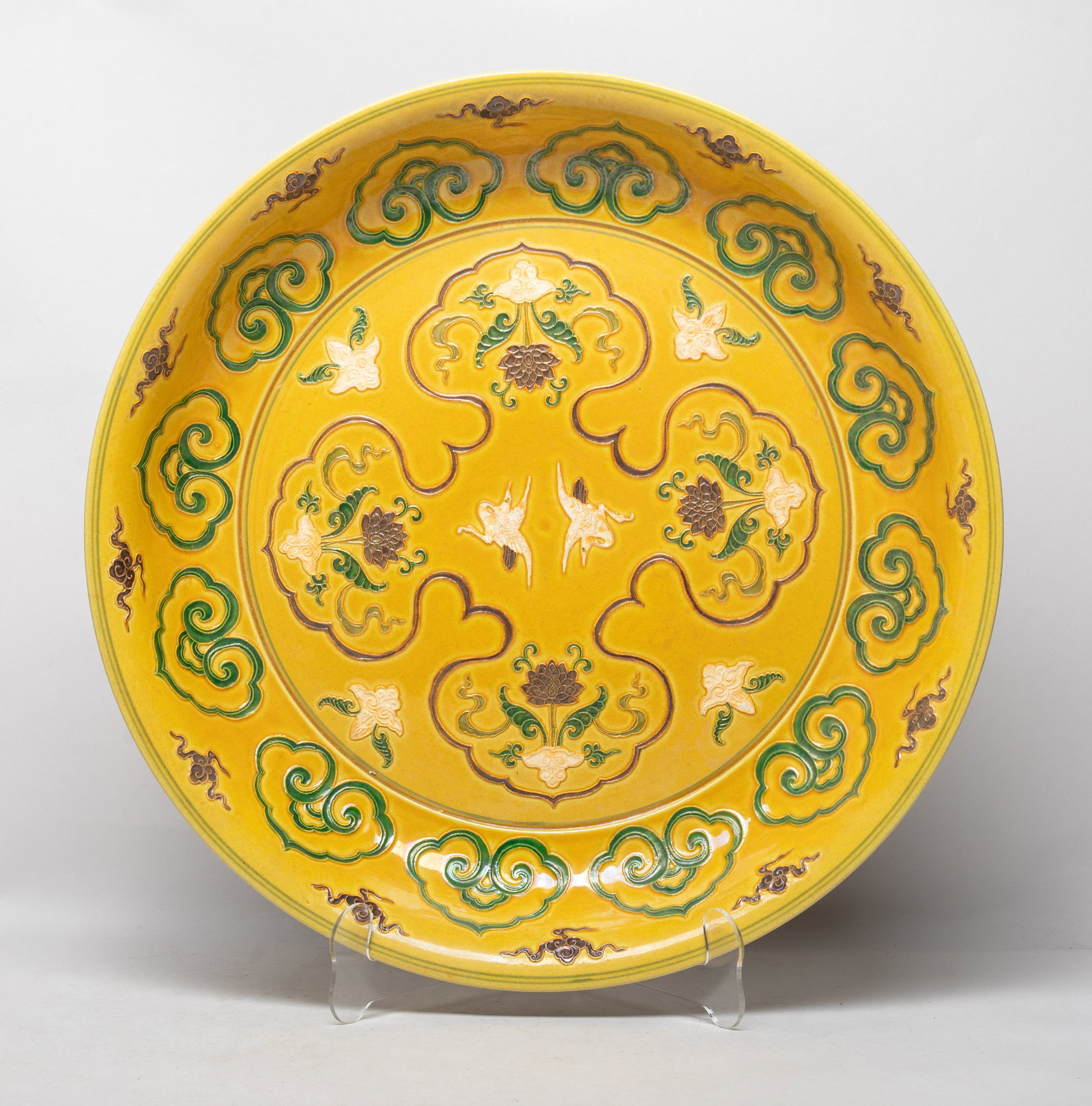 Large Chinese Export Porcelain Charger: The charger interior centre carved with ruyi heads enclosing lotus and cranes, the sides with ruyi heads and clouds around the inside and out, all against yellow glazed background. Approx. 15.5*2.5 in