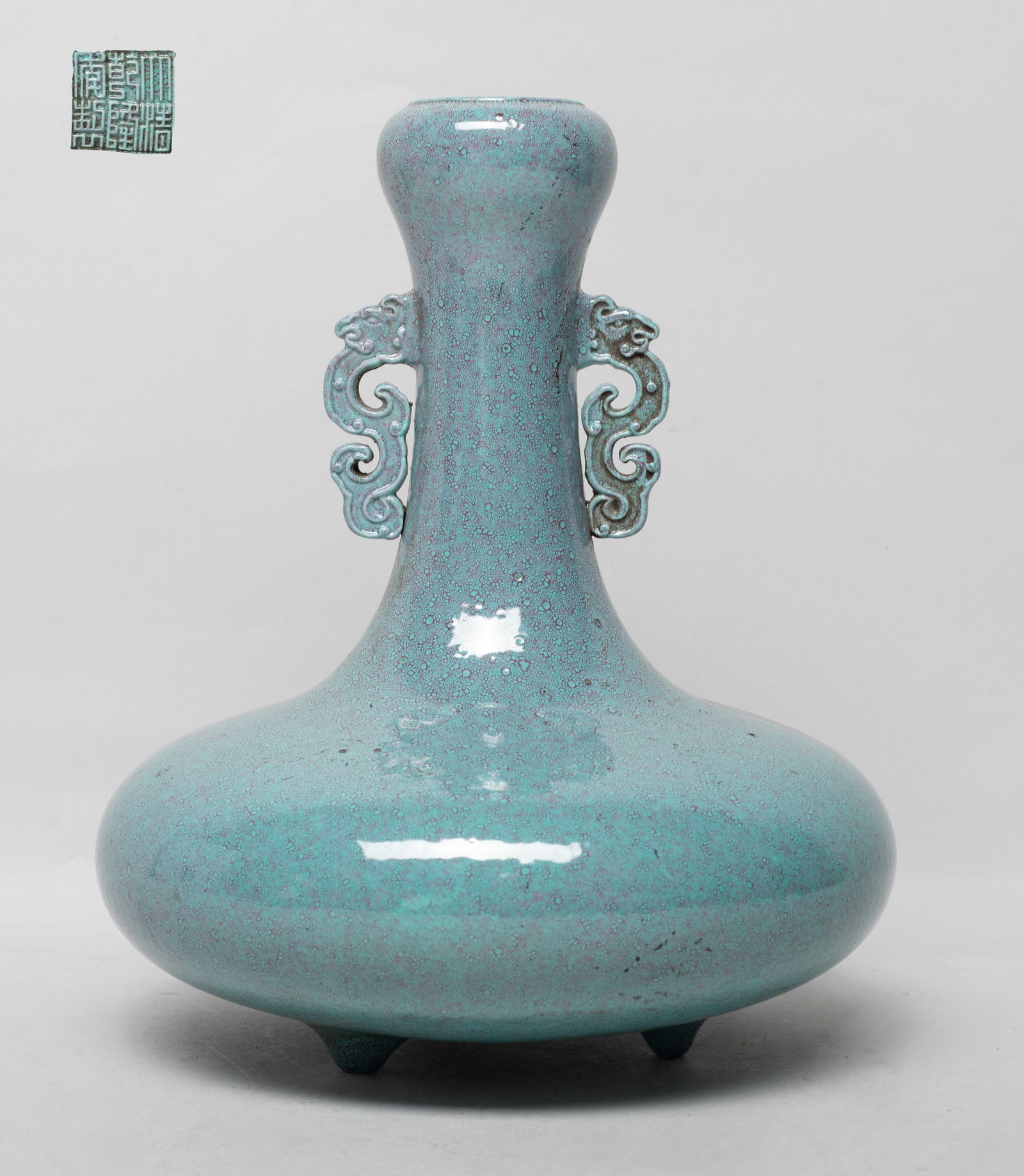 Chinese Flambe Glazed Porcelain Vase: The compressed globular body rising to a tall slender neck and a garlic mouth, flanked by a pair of stylized dragon handles, resting on three short tapered feet, the exterior covered in turquoise glaz