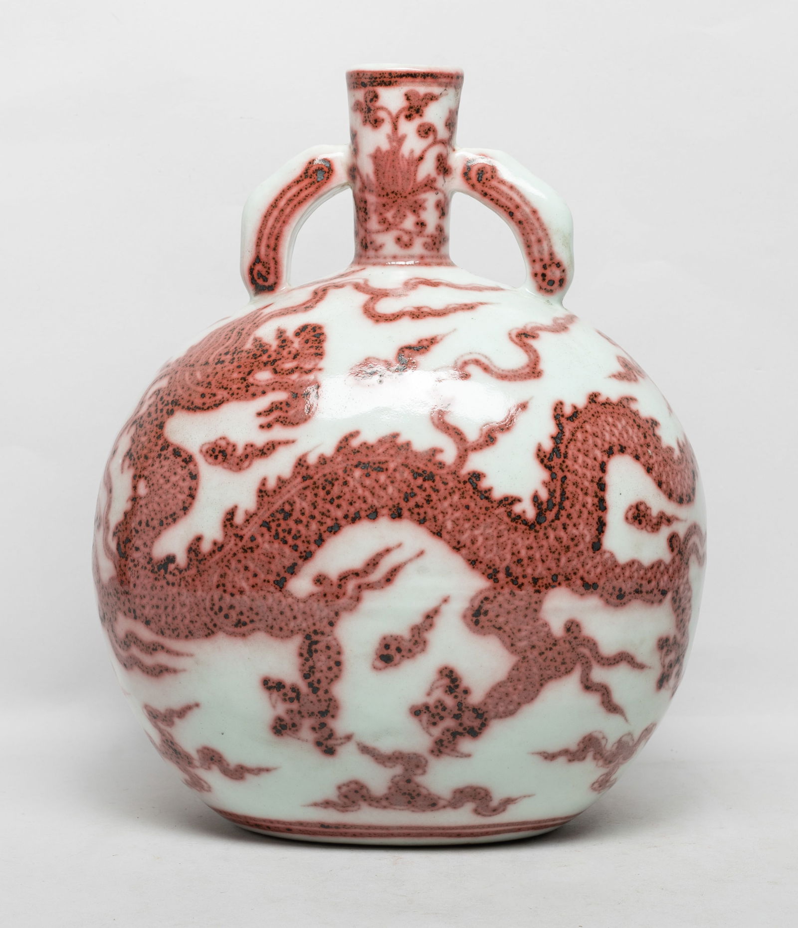 Chinese Copper Red Glazed Porcelain Vase: The rounded body painted on either side in copper red with a ferocious dragon amidst scrolling clouds, the neck with lotus scrolls flanked by two handles. Approx. 11*8.7*6.2 inch.
