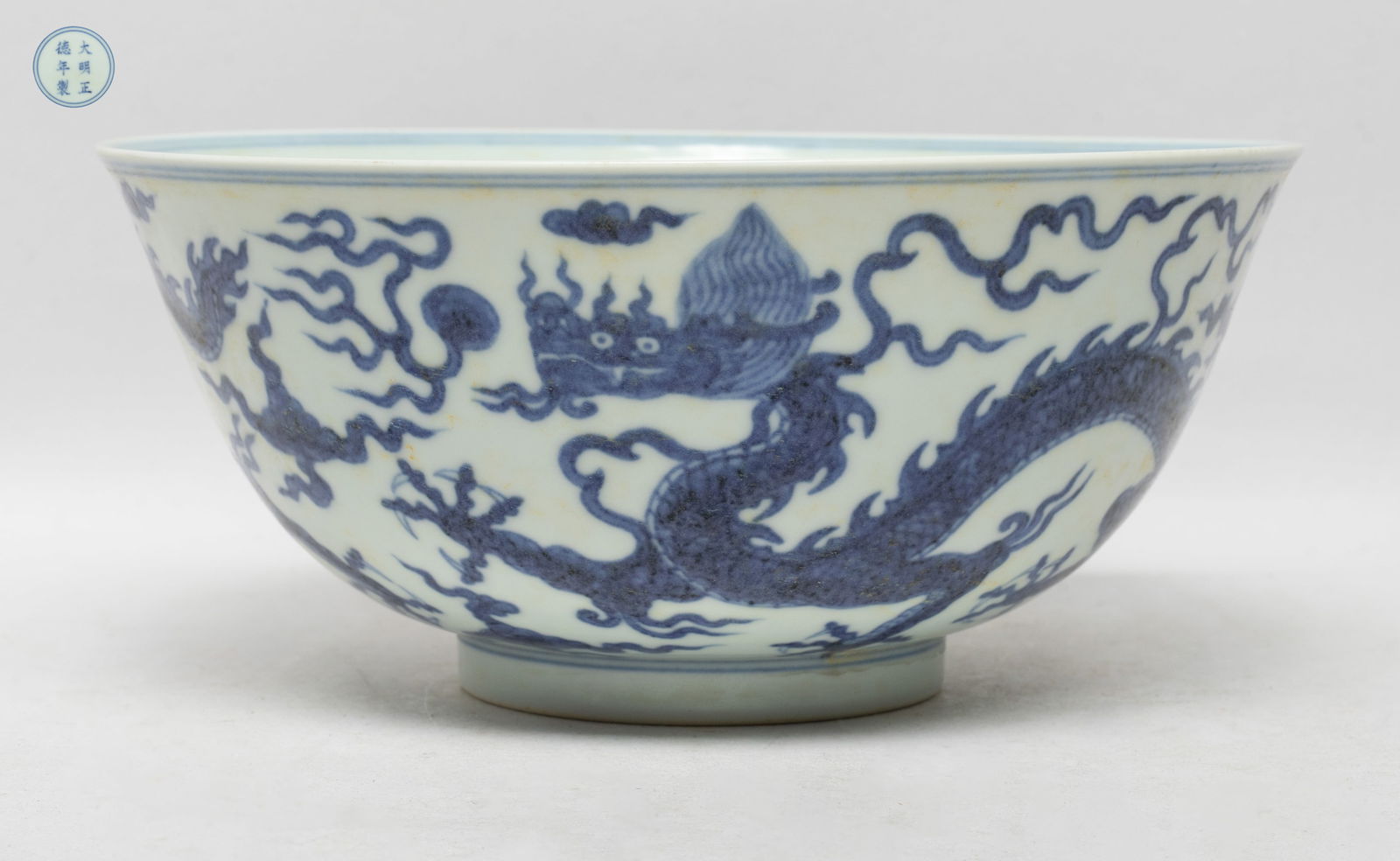 Chinese Blue & White Porcelain Dragon Bowl: The bowl exterior painted with five-clawed dragons chasing flaming pearls amidst clouds, the interior centre decorated with a stylized character framed by a band of ruyi heads, the bottom marked with