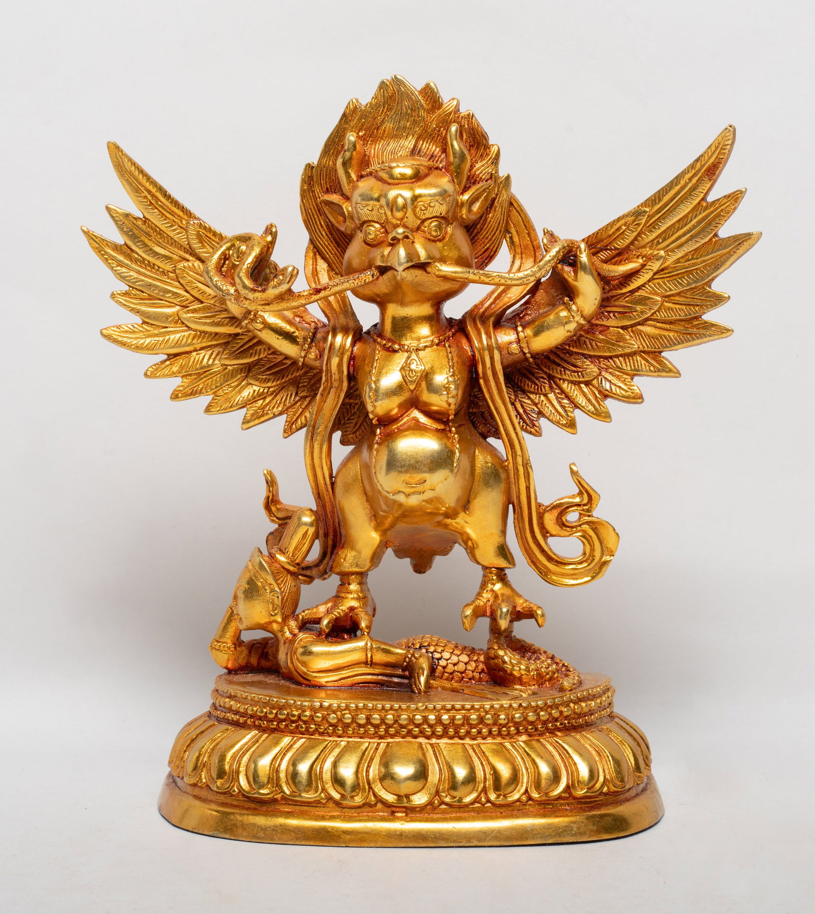 Chinese Sino-Tibetan Bronze Sculpture: the horned zoomorphic bird-headed deity standing with flexed legs holding up the head and tail of a naga with its snake's body passing through his beak, an emblem of flaming jewels on the crown of his