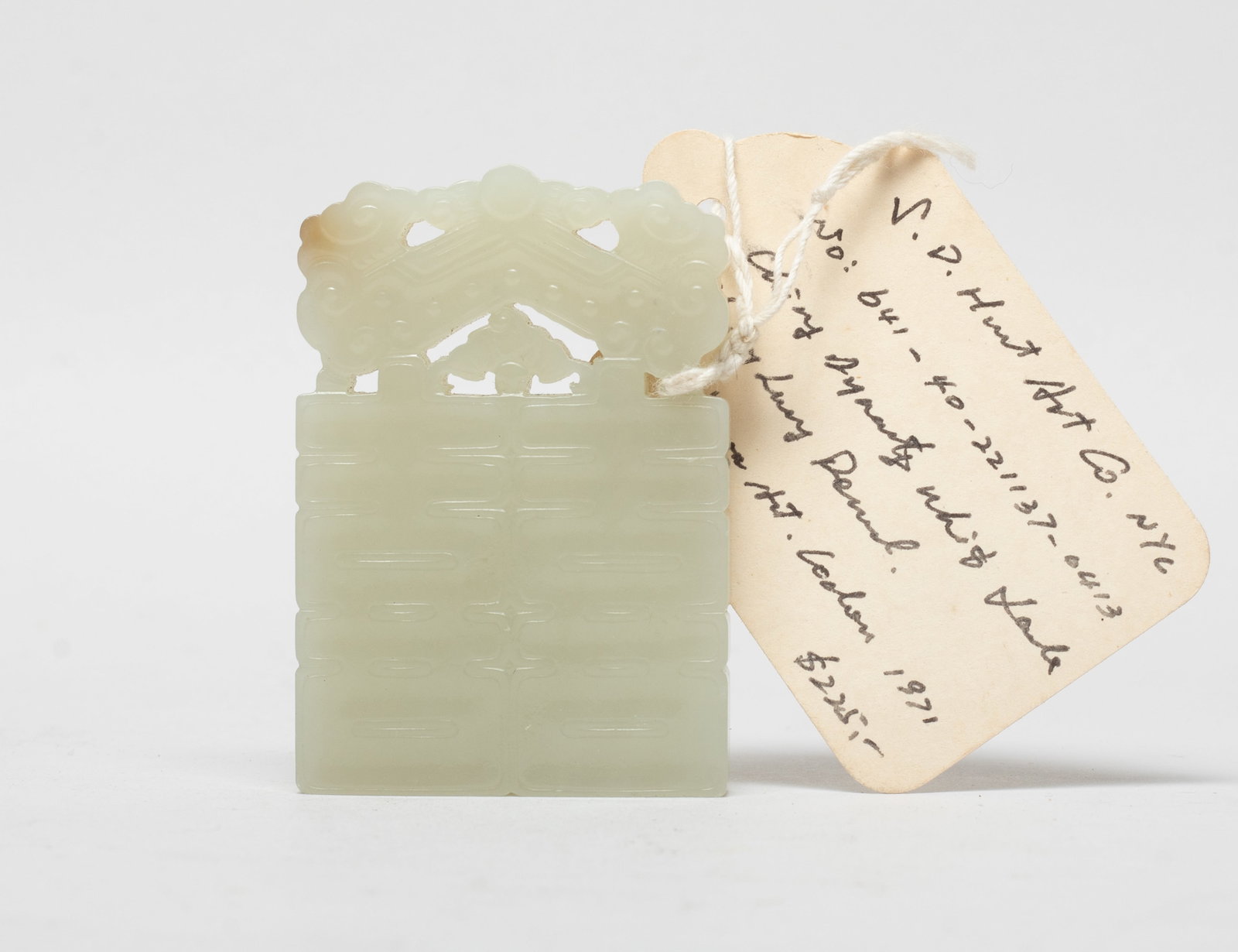 Chinese Export Jade Carved Pendant: Deftly carved as a double happiness symbol, surmounted with a traditional instrument and a bat, the stone of pale celadon tone with light russet inclusions. Approx. 2.45*1.7 inch.