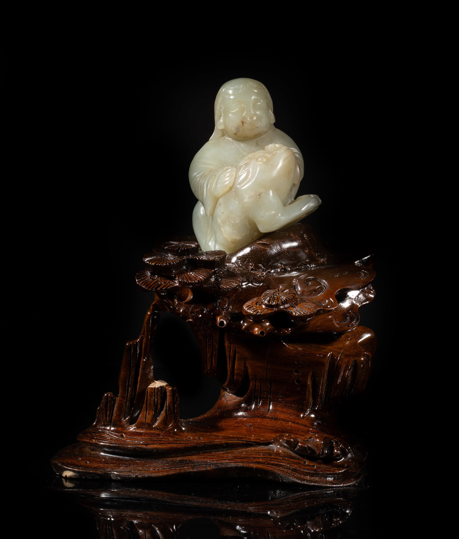 Chinese Jade Carved Liuhai on Wood Base: Carved as Liuhai carrying a large toad, the stone of mottled pale celadon tone with cloudy inclusions, with a tall wood base carved with pine tree and rock. Approx. 2.85*2.5*2 inch (w/o base). The