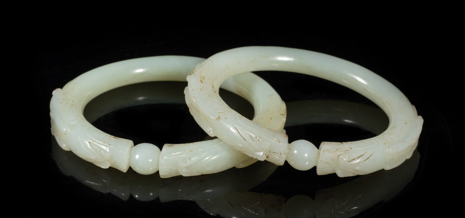 Two Chinese Ming Jade Dragon Bangles: Each finely worked in the form of two dragons sharing the same body facing each other at the top, both the mythical beasts fighting over a pearl, the stone of almost white tone with brown inclusions. 