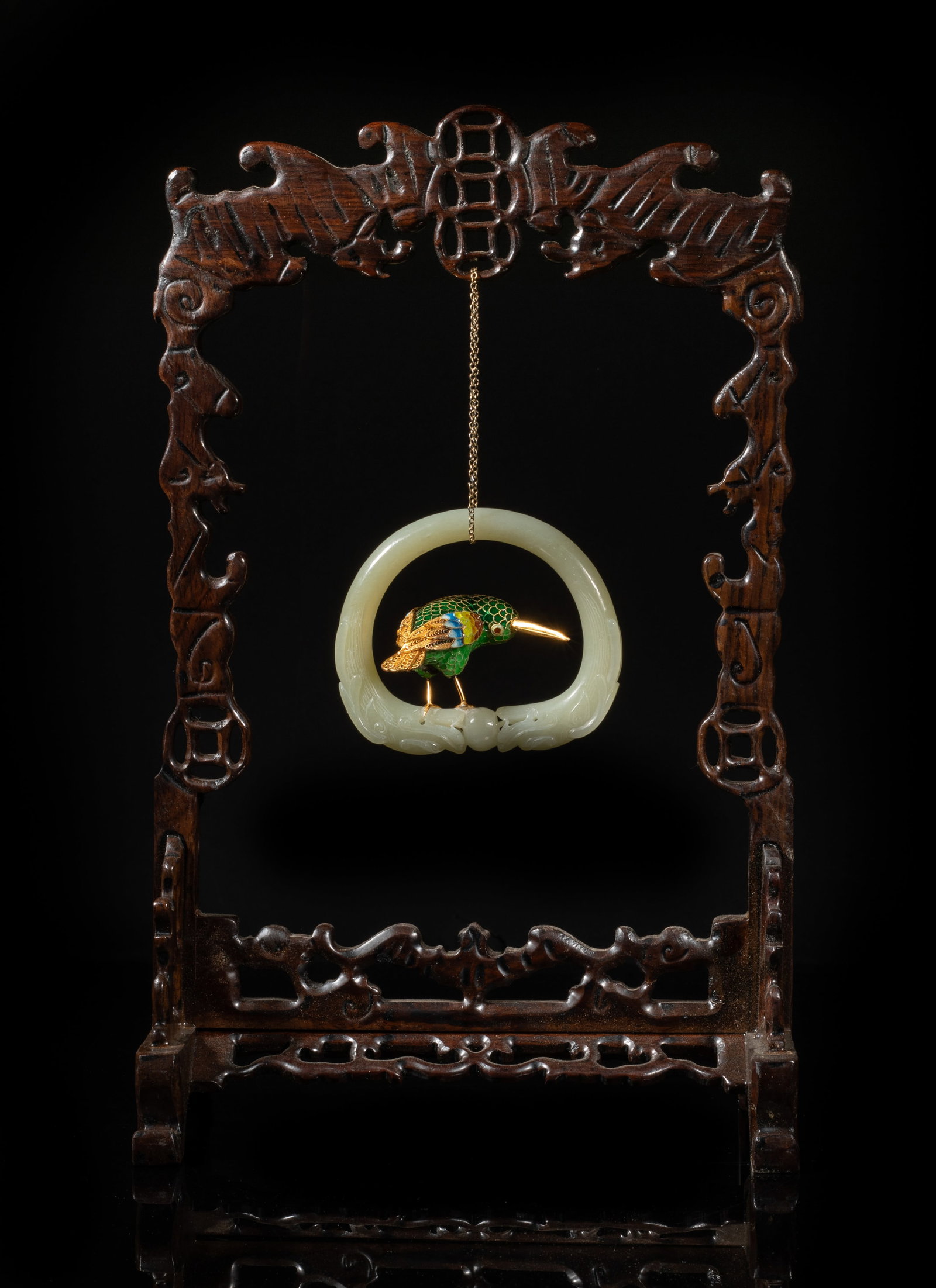 Chinese Gold on Sterling, Jade Wood Table Ware: Chinese jade bangle carved with a pair of dragons facing a ball, decorated with an enameled gold on sterling bird, suspended on a wood stand carved in openwork with bats and coins. Approx.