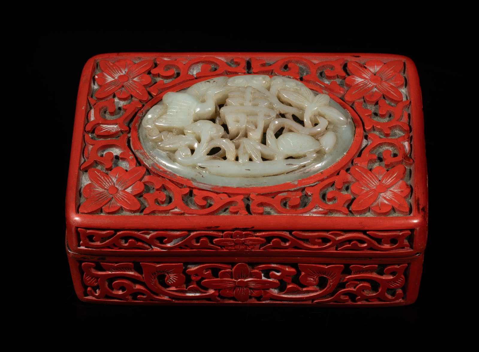 Chinese Cinnabar Box Inlaid Jade Plaque: Of rectangular section, carved with stylized flowers, inlaid with a jade plaque on the top, carved in openwork with crane, turtle, and lingzhi surrounding a shou character. Approx. 4.2*2.8*1.9 inch.
