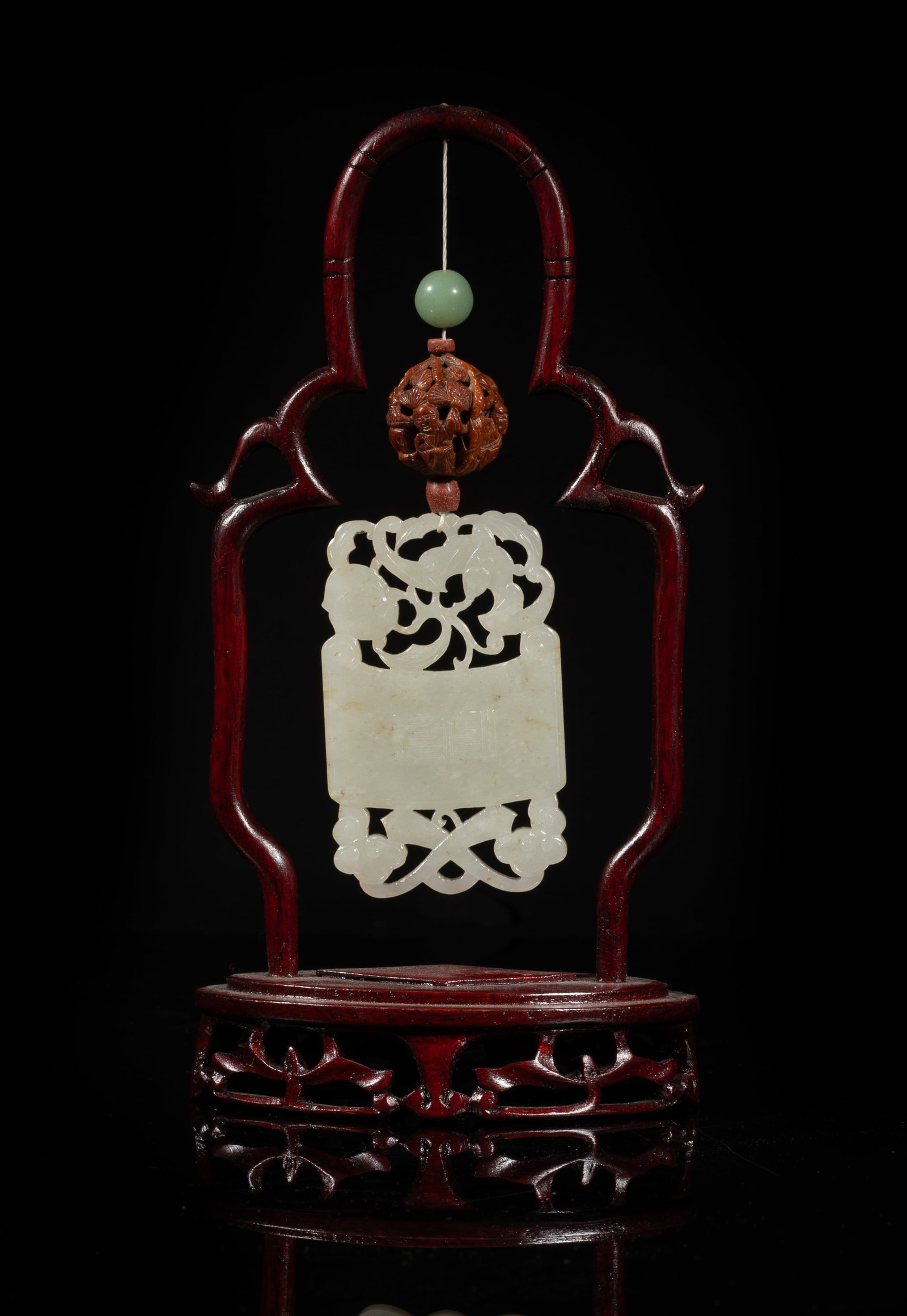 Chinese Jade Pendant on Wood Stand: Chinese jade pendant carved in openwork with bat and peach on the top and two crossed ruyi on the bottom, either side inscribed with two characters, the stone of white tone with faint russet