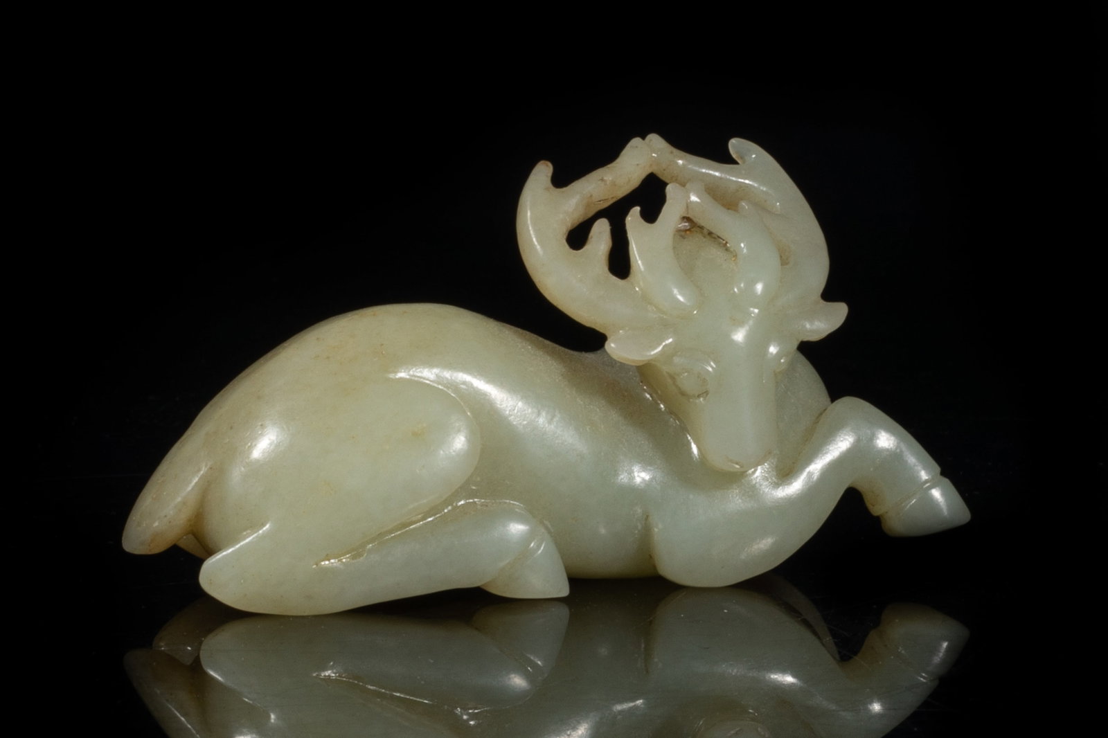 Rare Chinese Jade Carved Sculpture: The animal with its right front leg outstretched and the other three legs tucked beneath it, its horned head curled to the right, incised with two flowers on the haunch, the stone of pale celadon tone