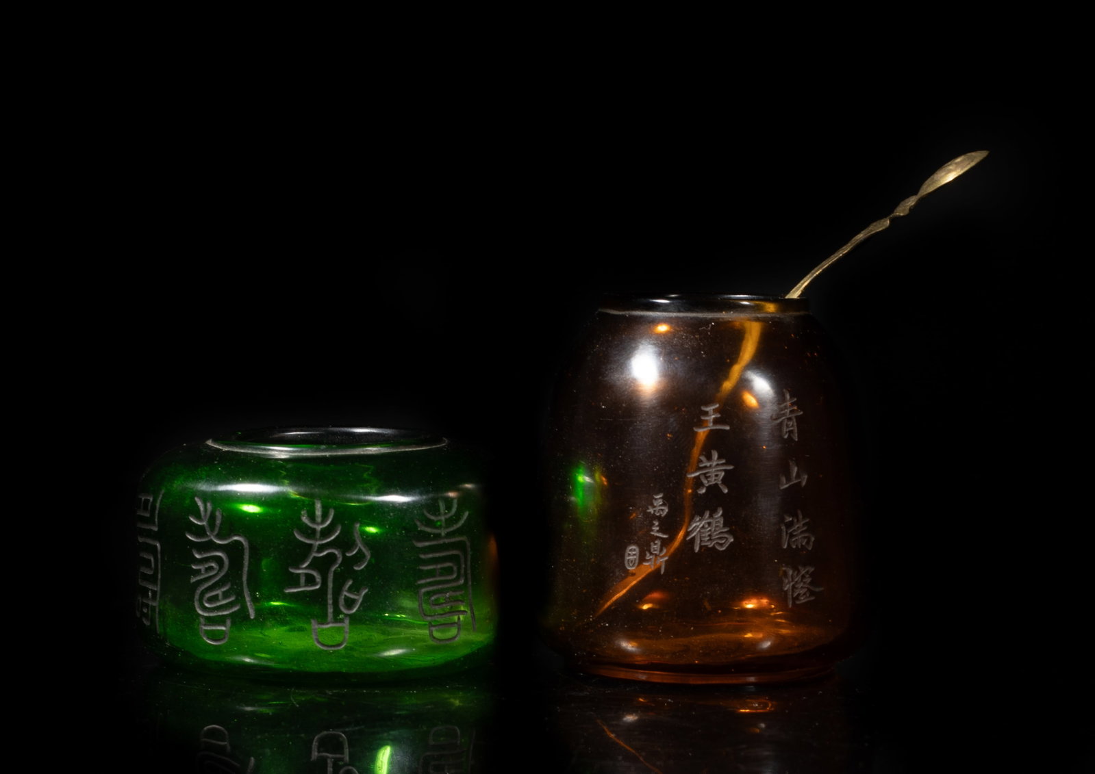 Two Chinese Peiking Glass Water Pots: The brown glass water pot incised with a boy and a bat, inscribed with related poems, the other green glass pot incised with ancient characters, each bottom marked with four characters, with a spoon.