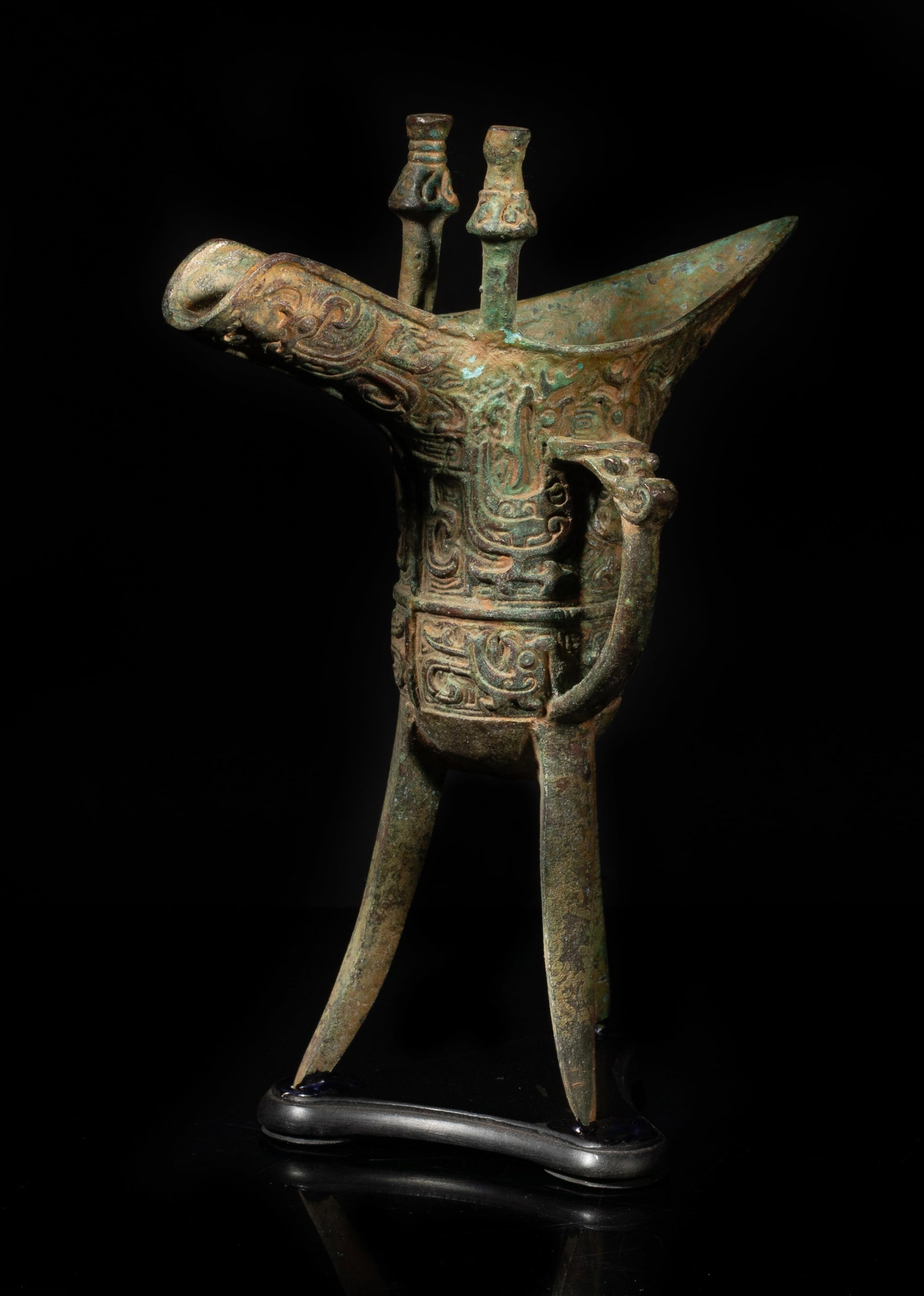 Chinese Bronze Tall Cup w/ Wood Base: The cup body cast with archaistic beasts, a loop handle topped with a bovine head, near the spout surmounted with two capped finials, with a wood base. Approx. 7.8*5.7*2.9 inch (w/ base).