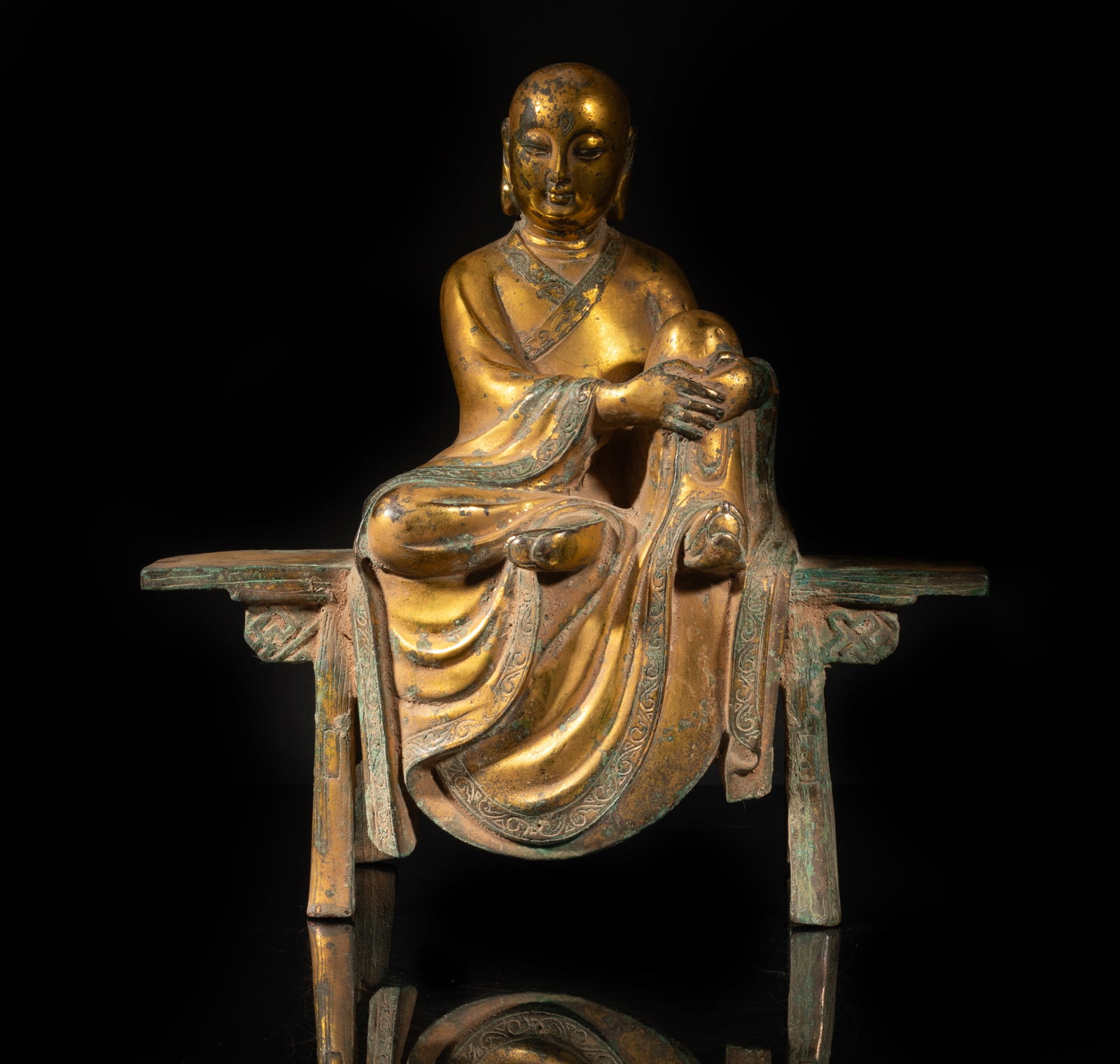Large Chinese Gold on Bronze Buddha: Cast as bald Buddha seated on a long bench, dressed in a long flowing robe, the rounded face flanked by a pair of pendulous ears, the forehead incised with an eye. Approx. 11.2*11.2*4.4 inch.