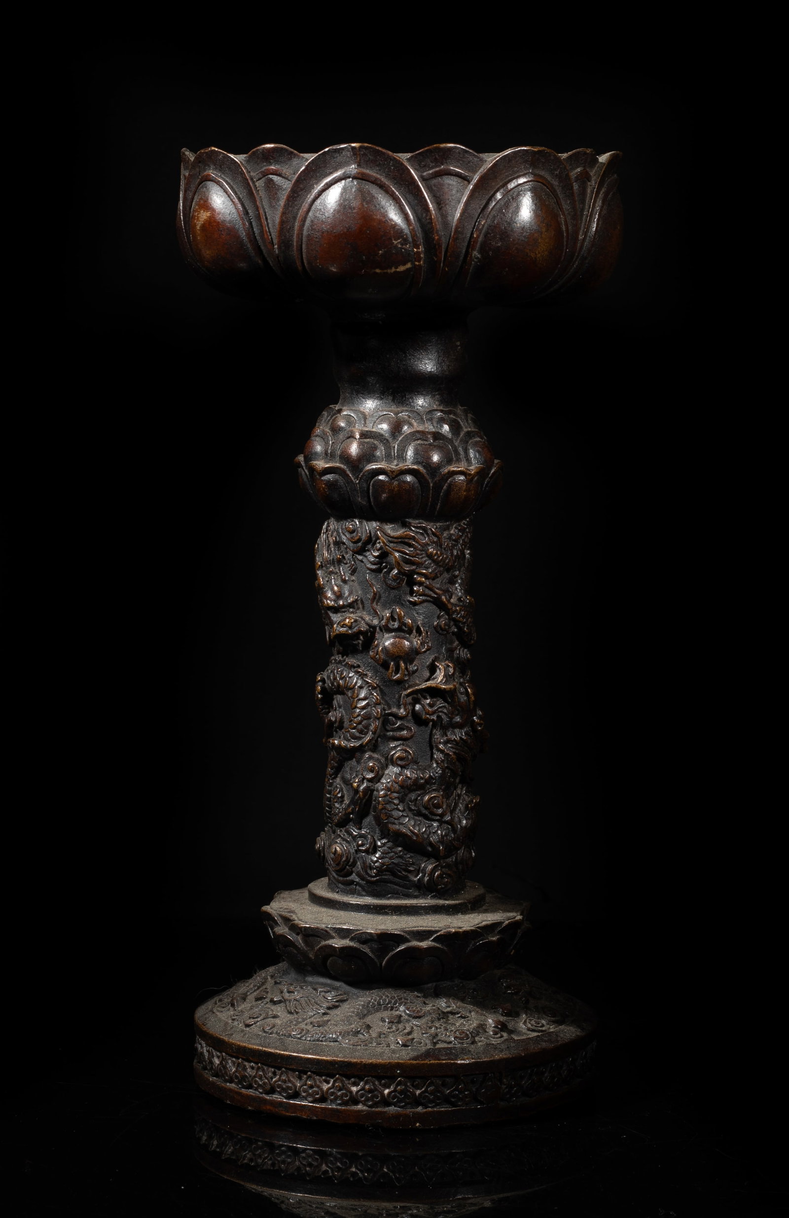 Rare Tall 19th Japanese Bronze Candlestick: The lotus form candlestick holder supported on a post carved with dragons sinuous amidst clouds below a lotus, the circular base carved with similar patterns, the bottom marked with four characters. A