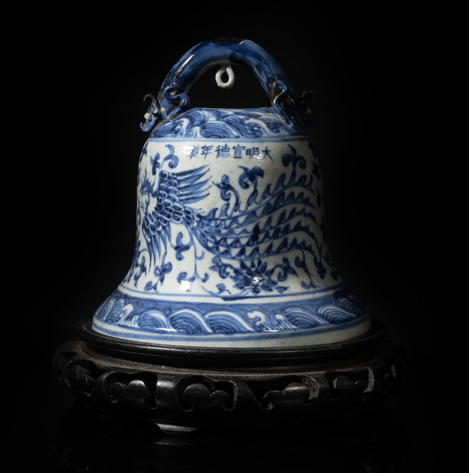 Chinese Blue & White Porcelain Bell w/ Wood Base: The bell exterior painted with two phoenixes among lotus sprays, between bands of waves, the handle moulded with two beast heads, with a wood base. Approx. 6.5*6.2 inch (w/o stand).