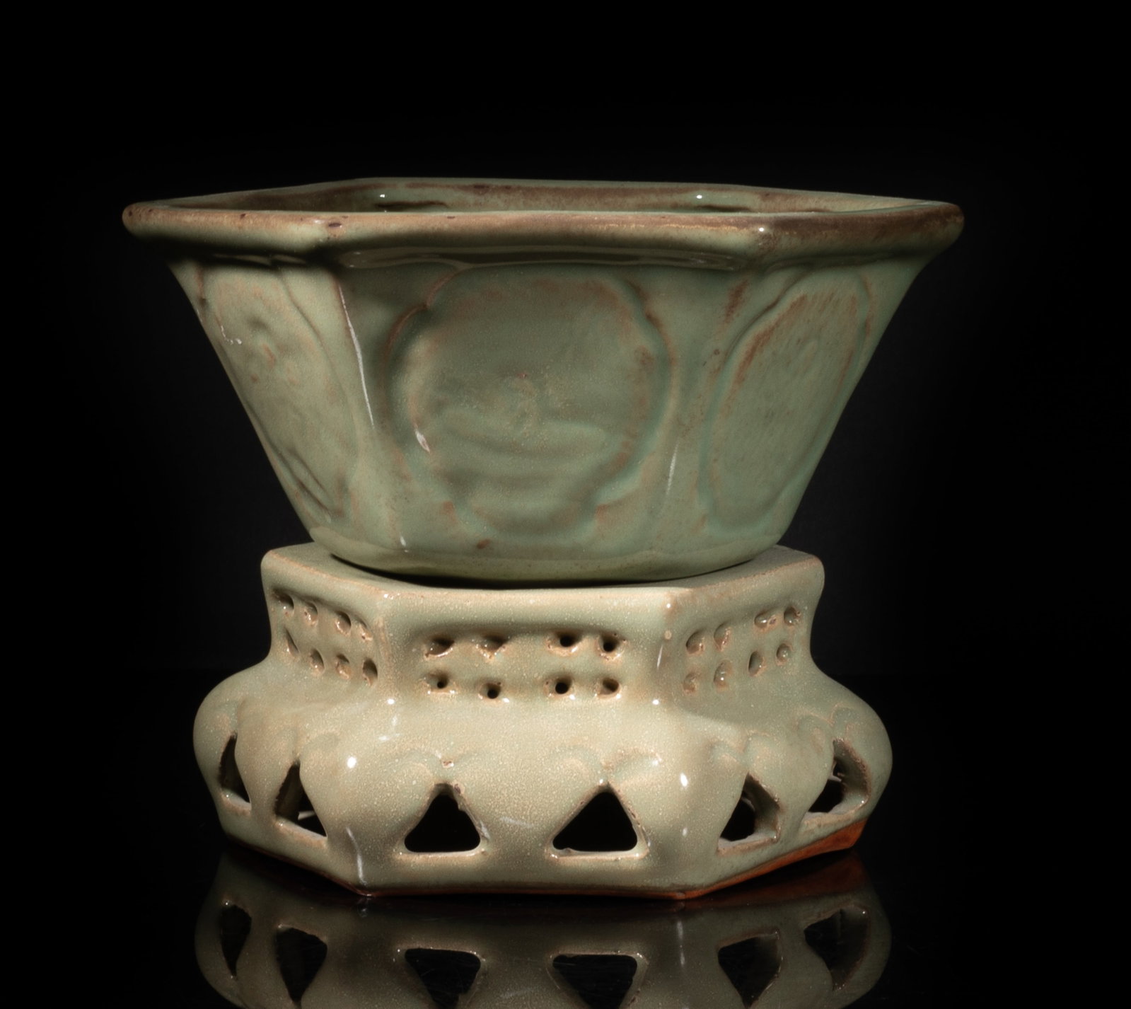 Estate Chinese Longquan Porcelain Flower Pot: The pot and openwork stand of hexagonal section, each side of the pot carved in low relief with a panel of figural scene, each covered overall with mottled celadon glaze save for the unglazed bottom.