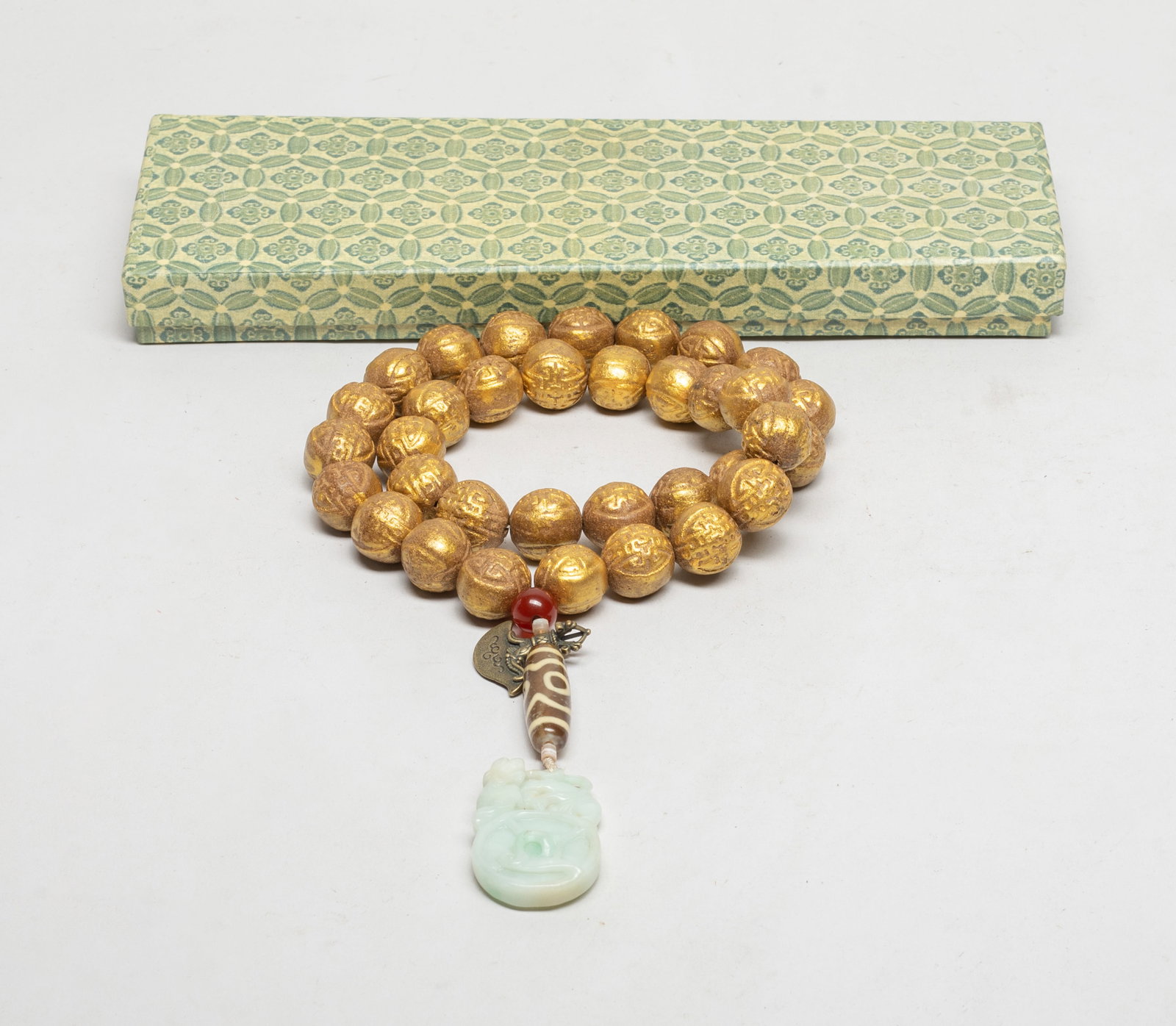 Chinese Gilt Mixed Agarwood Hexiang Prayer Beads: A string of Chinese gilt mixed agarwood hexiang carved prayer beads, slightly fragrant, suspended with beads, a metal pendant, and a stone pendant carved as a beast on a coin. Approx. 0.75 inch D