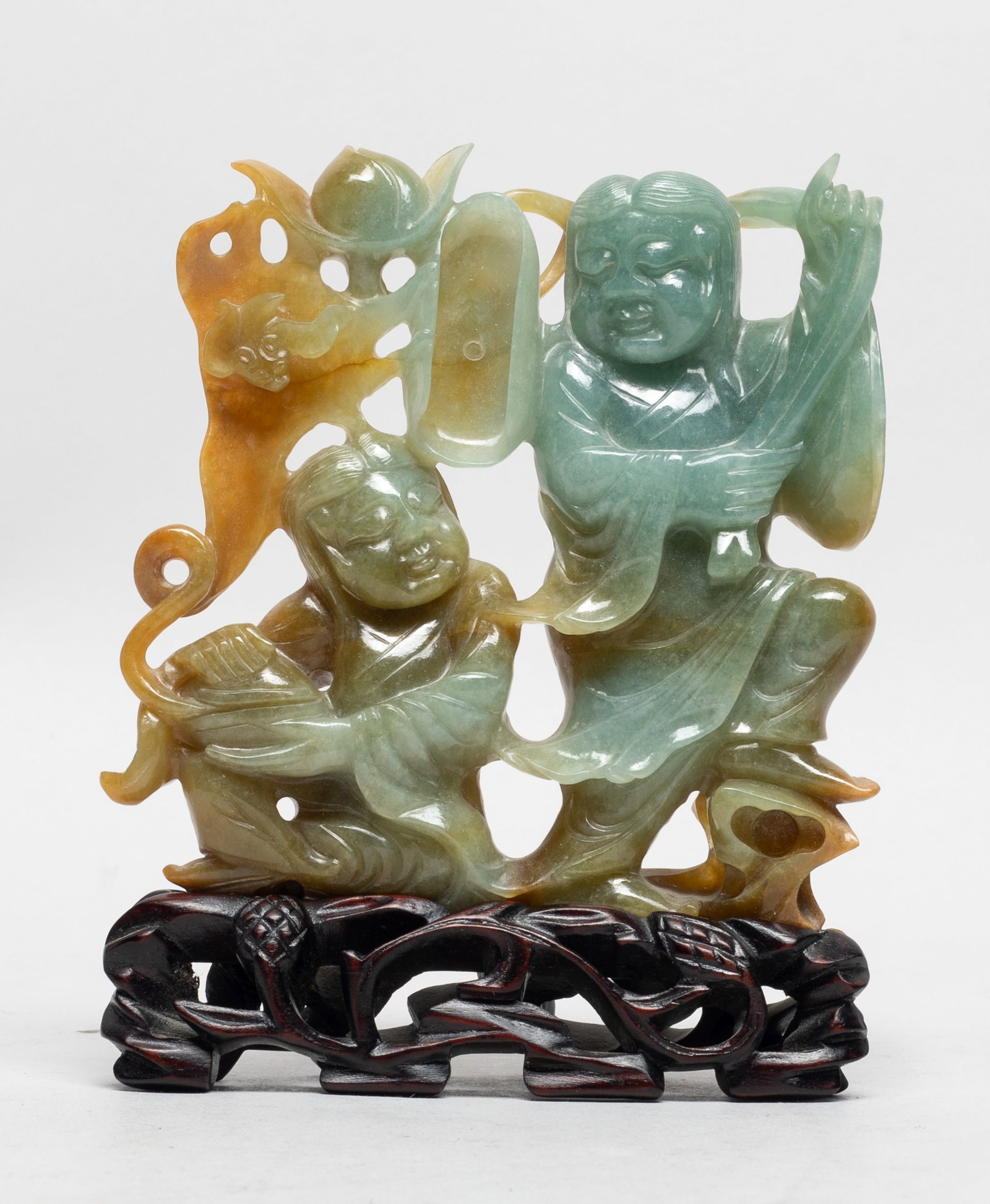 Chinese Jade Jadeite Sculpture of Hehe: Carved from a celadon and russet stone as two standing boys back to back, one holding a box spraying clouds, a bat and a peach atop, the other holding a long stem issuing a lotus leaf over their