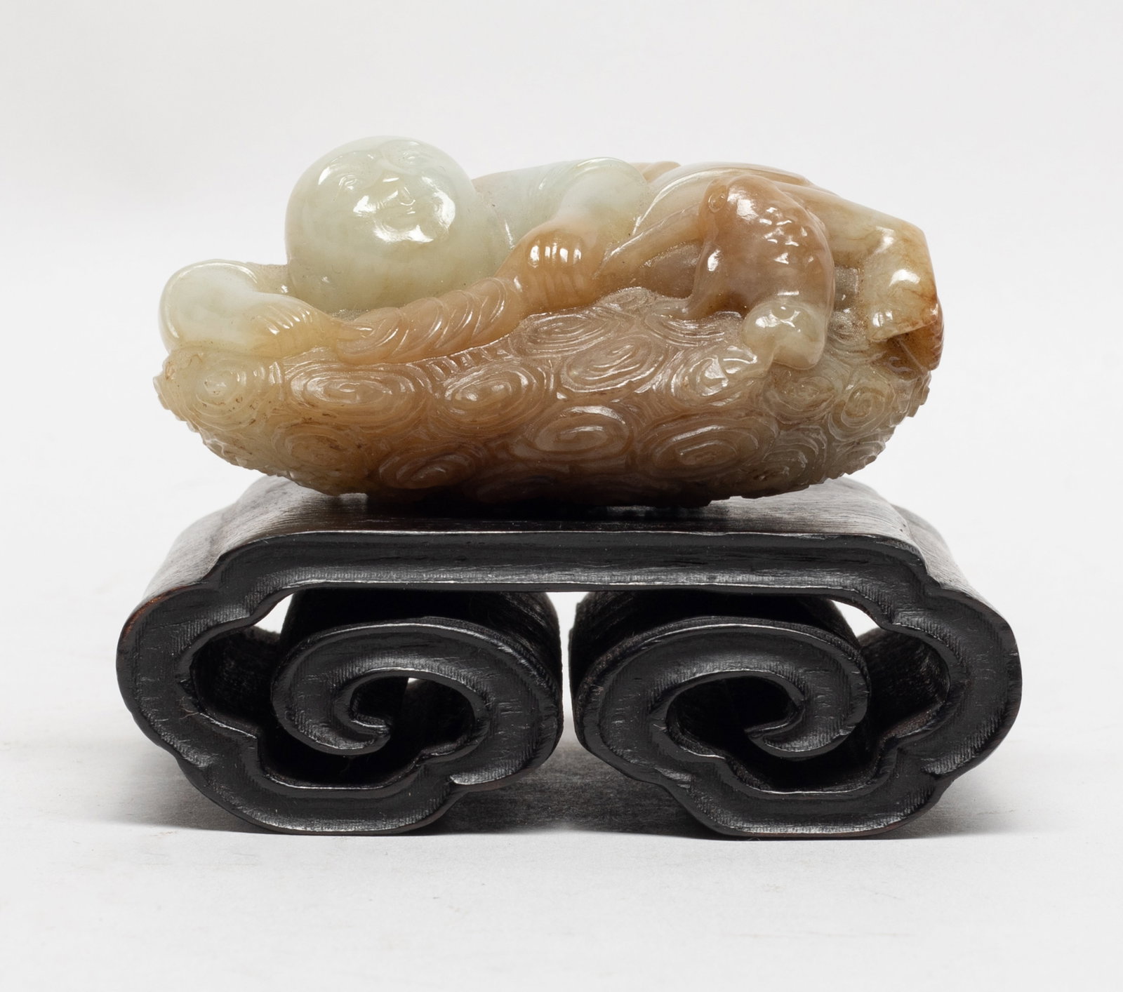 Chinese Russet Jade Sculpture w/ Wood Base: The russet jade pebble carved as Liuhai lying on scrolling clouds, his hands holding a string of coins, a toad biting the end of string, with wood stand. Approx. 3.55*2.55*1.75 inch (w/o stand). The E