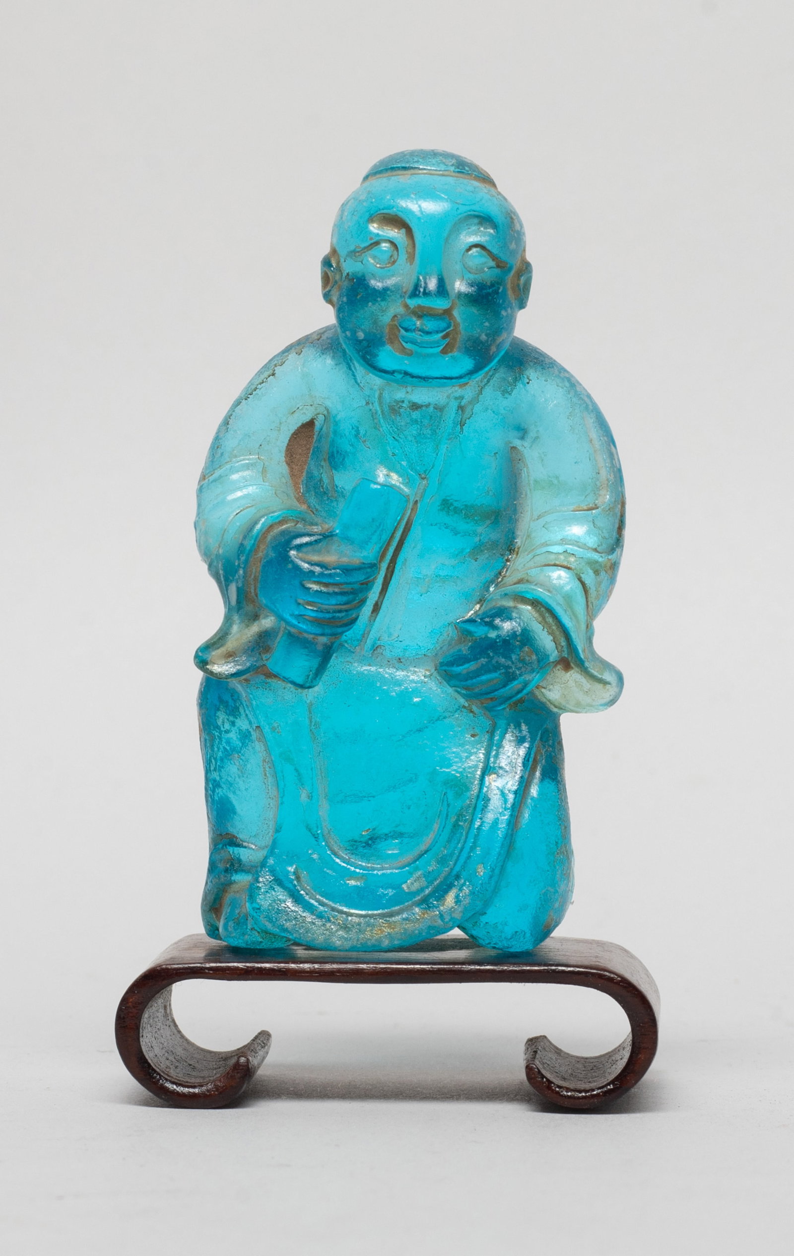 Rare Chinese Glass Figure w/ Wood Base: Chinese blue glass carved figurine, dressed in a long robe and holding a scroll book in hand, with a wood base. Approx. 2.6*1.4*0.9 inch (w/o base). The Estate of the K. F. Chung. HK. 1997.
