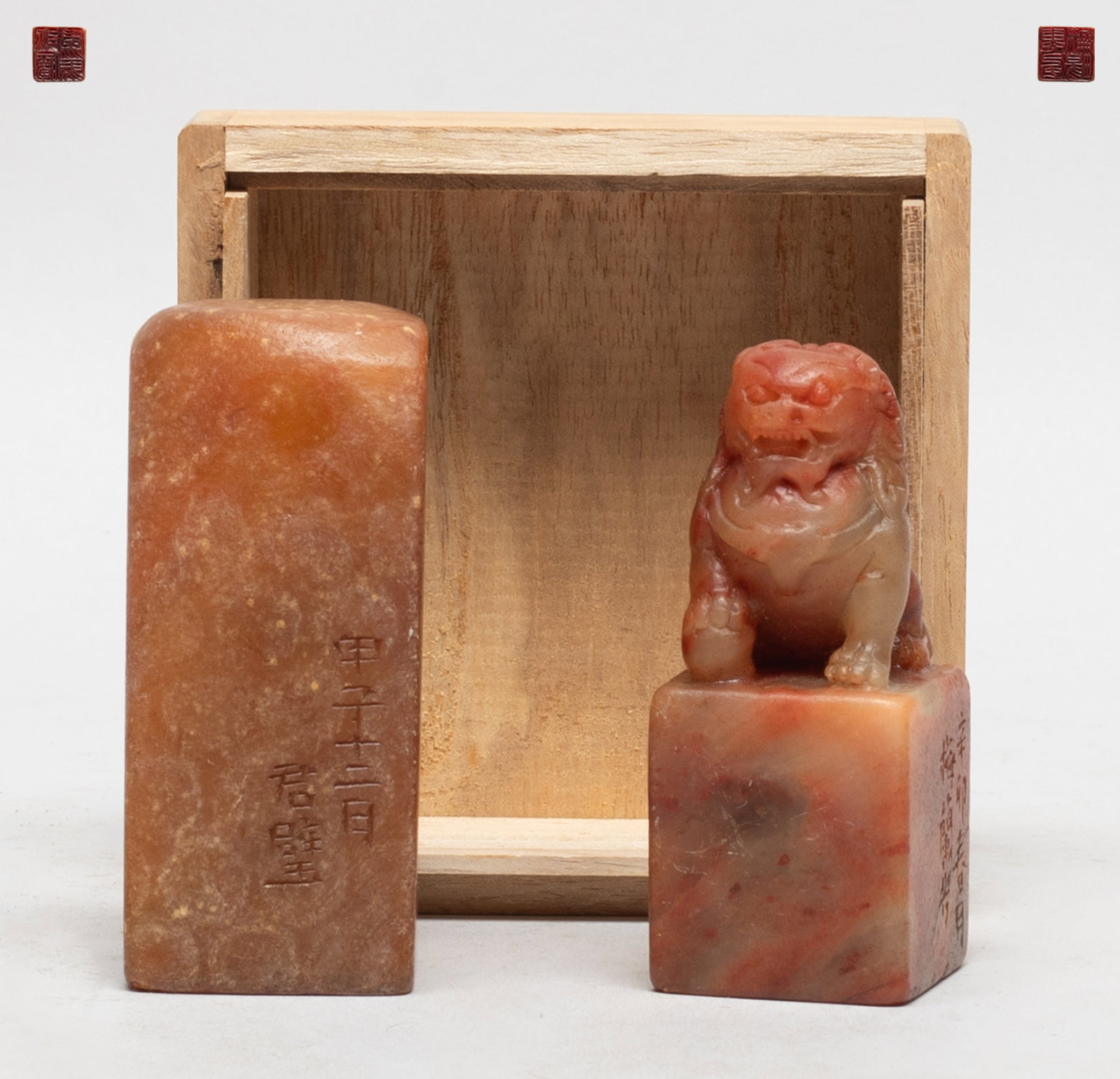 Two Chinese Shoushan Stone Seals: Both seals of square section, the smaller seal carved with a crouching foo dog on the top, with a lidless case. Approx. 3.25*1.4*1.3 inch (larger seal).