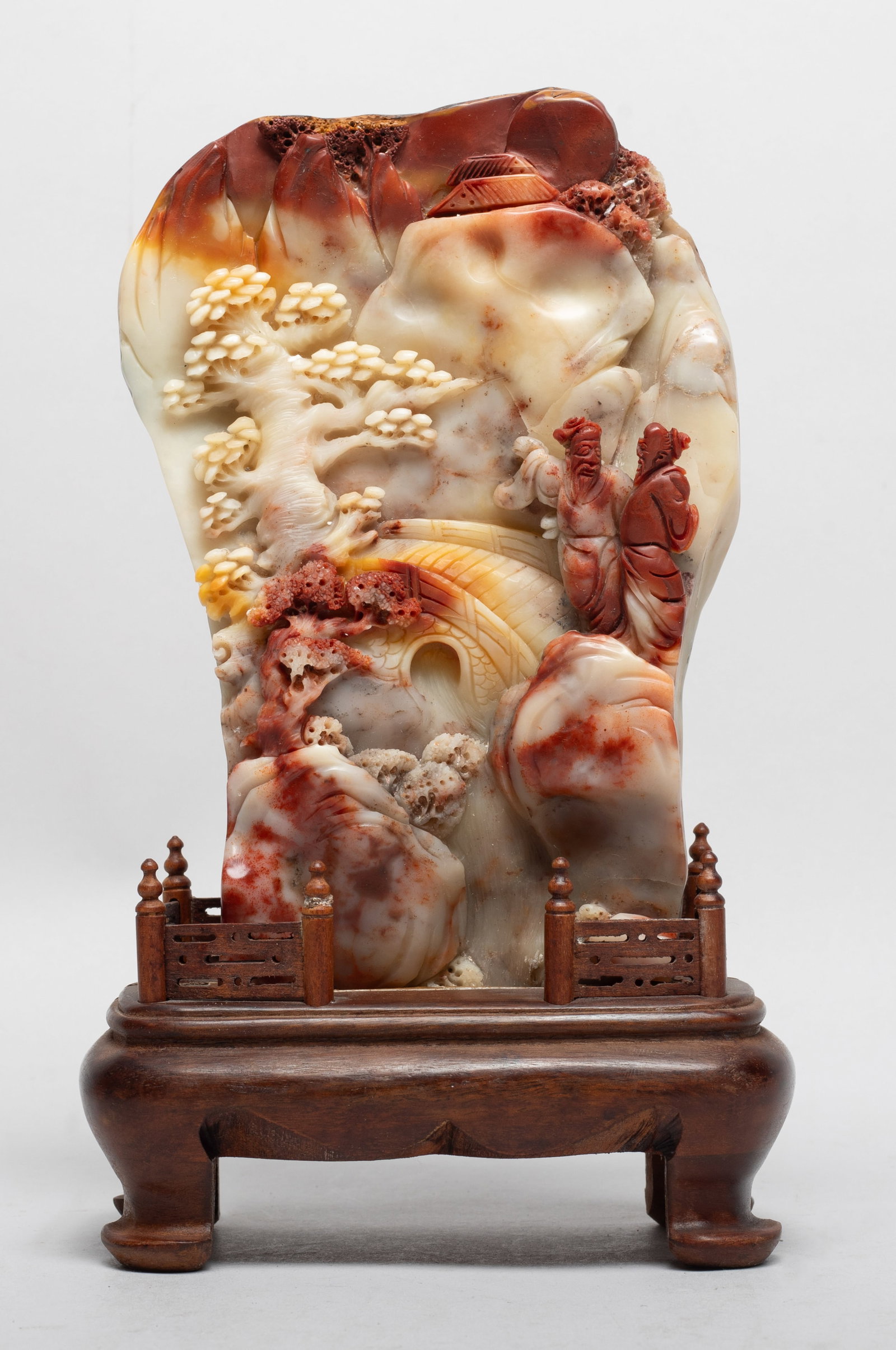 Estate Chinese Shoushan Stone Sculpture: The boulder of irregular mountain form, deftly carved in various levels of relief depicting two scholars standing on a rocky ledge towards a bridge, all set amidst a mountainous landscape dotted with