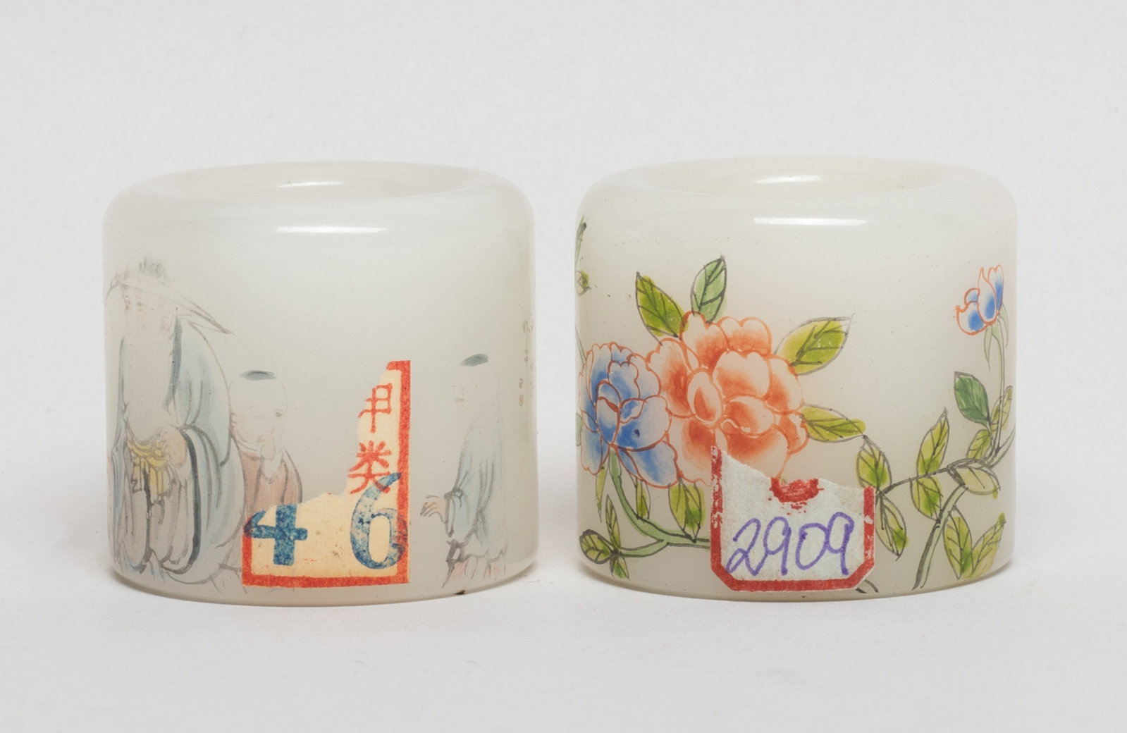 Two Chinese Peiking Glass Thumb Rings: One ring painted with blossoming flower stems, marked with four characters, the other painted with an old man and four boys. Approx. 1.6*1.4 inch (larger). The Estate of the Consignment Store Closed