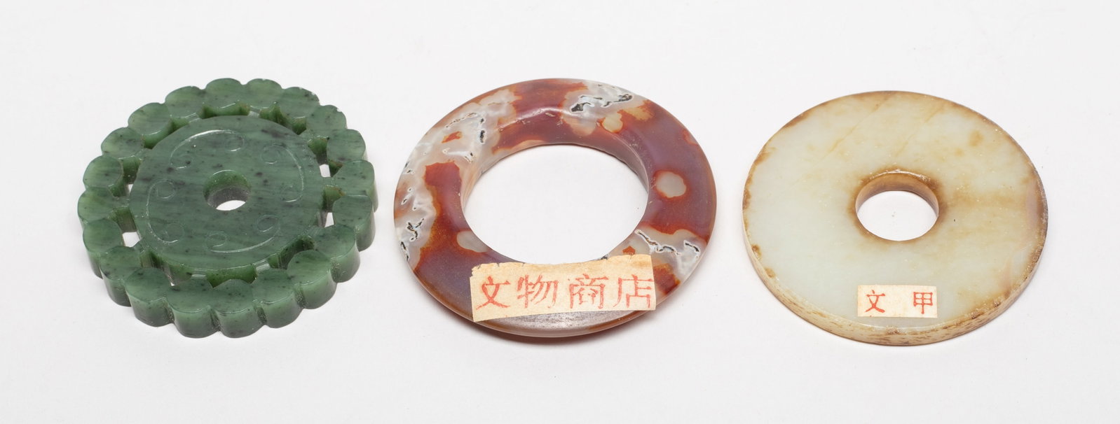 Chinese Jade, Moss Agate Carved Pendants: Including a moss agate carved huan, a russet jade bi, and a spinach jade pendant of disc form with a beaded frame. Approx. 2.2 inch D (largest). The Estate of the Store Moving Sale. Palm Springs. CA.