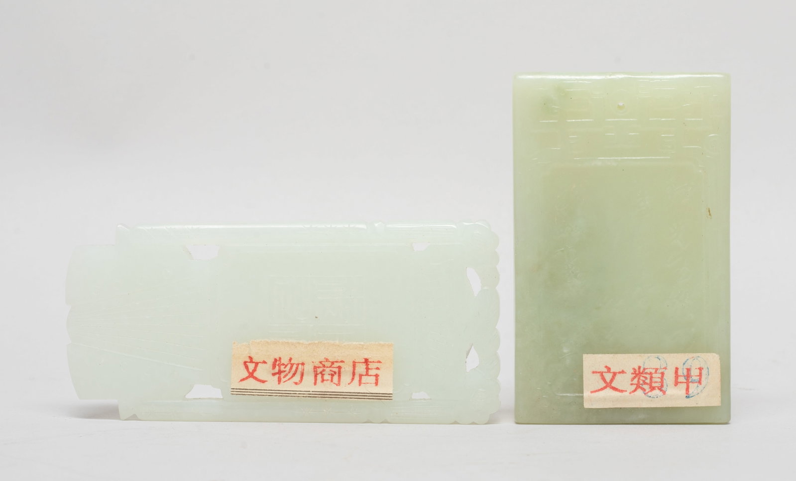 Two Chinese Export Jade Pendants: One white jade pendant carved on one side with a boy holding lingzhi and pomegranate, the reverse inscribed with four characters, the other pale celadon jade pendant carved on one side with an