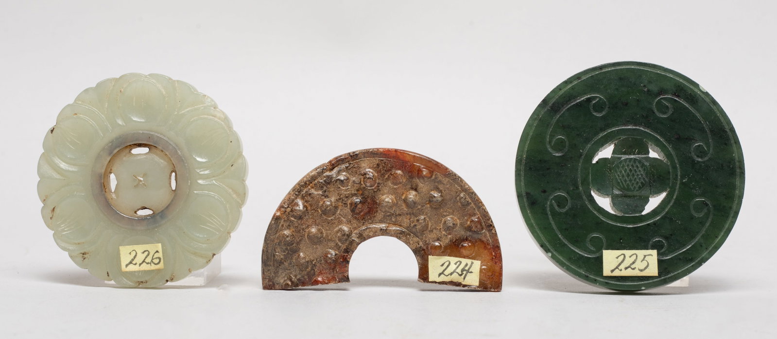 Three Chinese Jade Carved Pendants: Including a spinach jade pendant reticulated with a flower at the center, a pale celadon jade pendant carved of flower form, with a movable center, and a russet jade pendant of semicircular shape