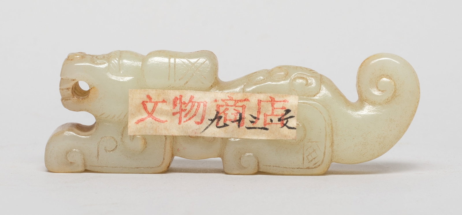 Chinese Jade Carved Pendant: Chinese russet jade pendant worked of recumbent beast form, the body detailed with archaic scrolls, drilled at the mouth for suspension. Approx. 2.97*0.97*0.58 inch. The Estate of Downtown, Los Angele