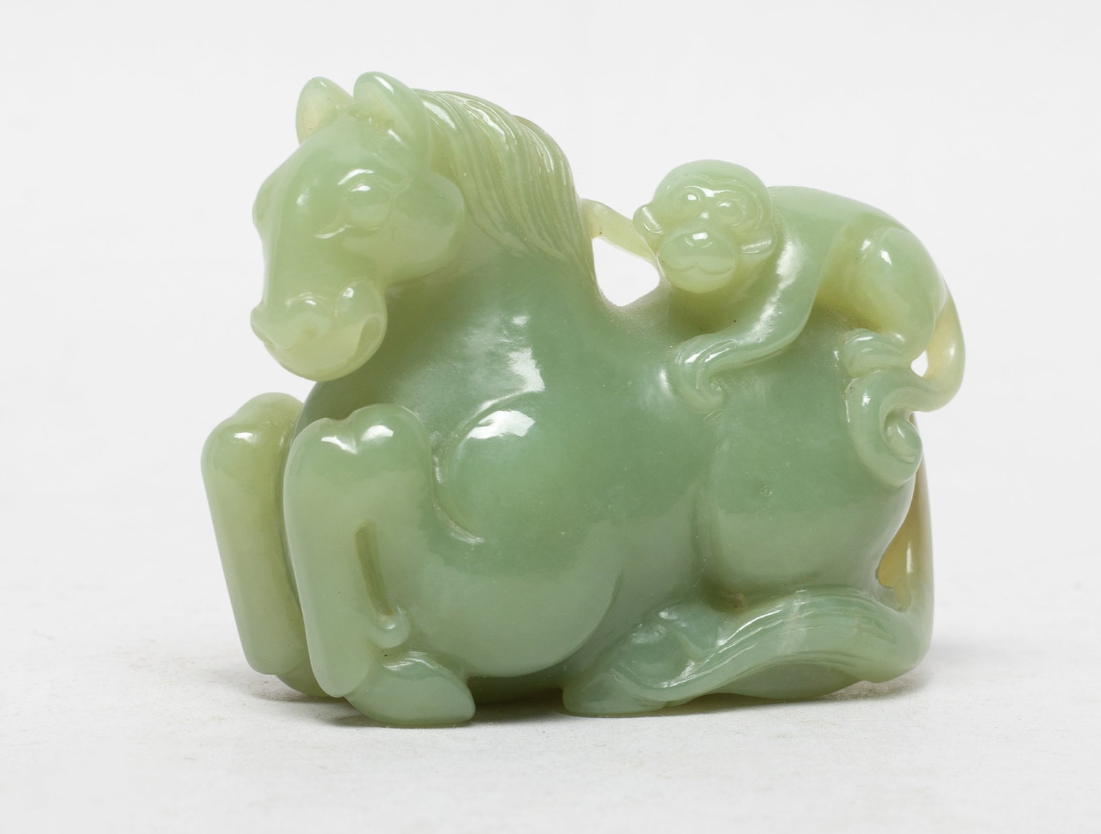 Chinese Pale Celadon Jade Horse & Monkey: Crisply carved as a recumbent horse with a monkey perched precariously on its back and clasping on the reins, the stone of pale celadon tone with some cloudy russet inclusions. Approx. 2.6*2*1.15