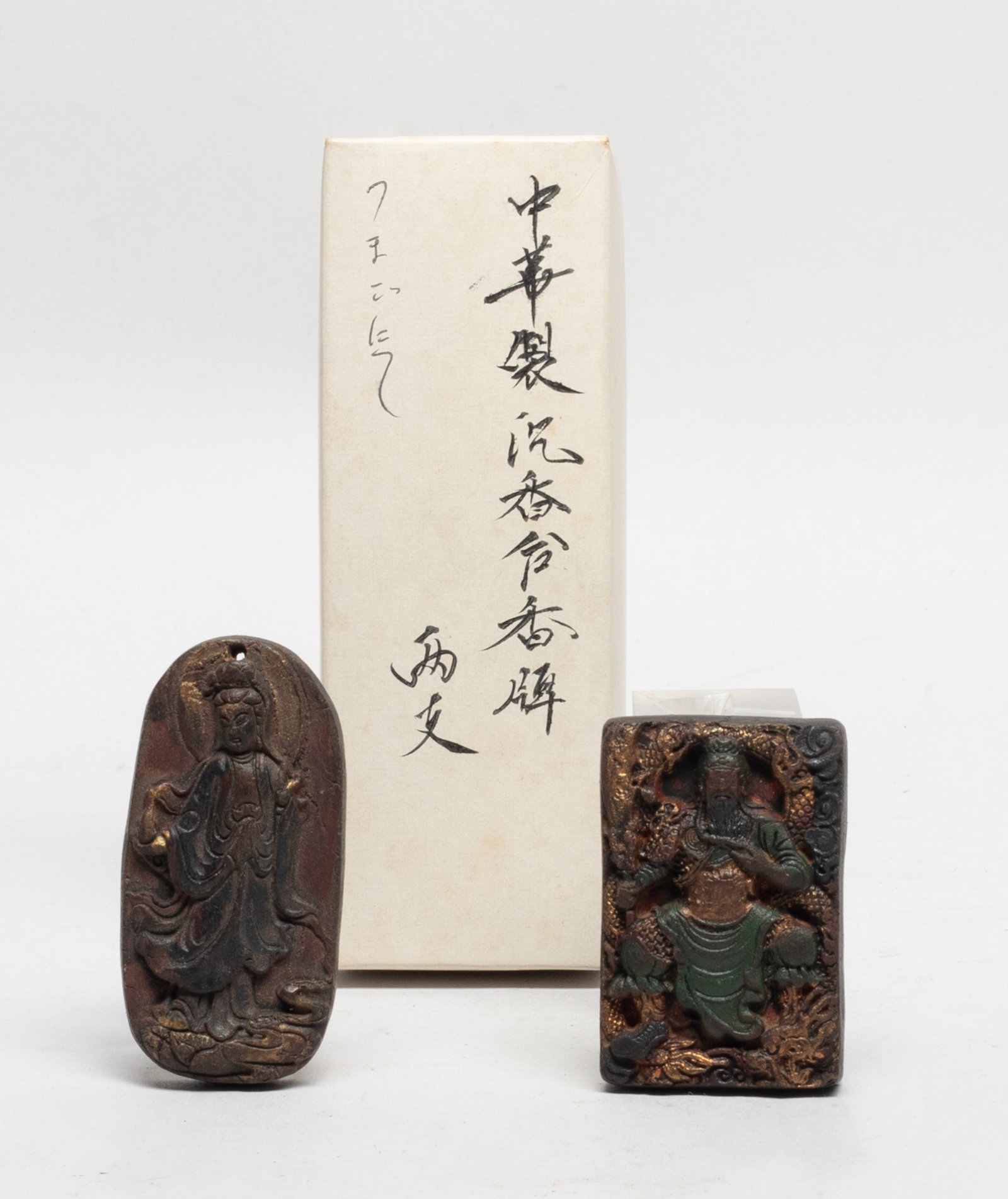 Two Chinese Mixed Agarwood Hexiang Pendants: One pendant carved with standing Kuanyin, the other carved with Kuandi surrounded by a dragon, slightly fragrant, with box. Approx. 43 gram (total weight), 2.53*1.27 inch (larger plaque).
