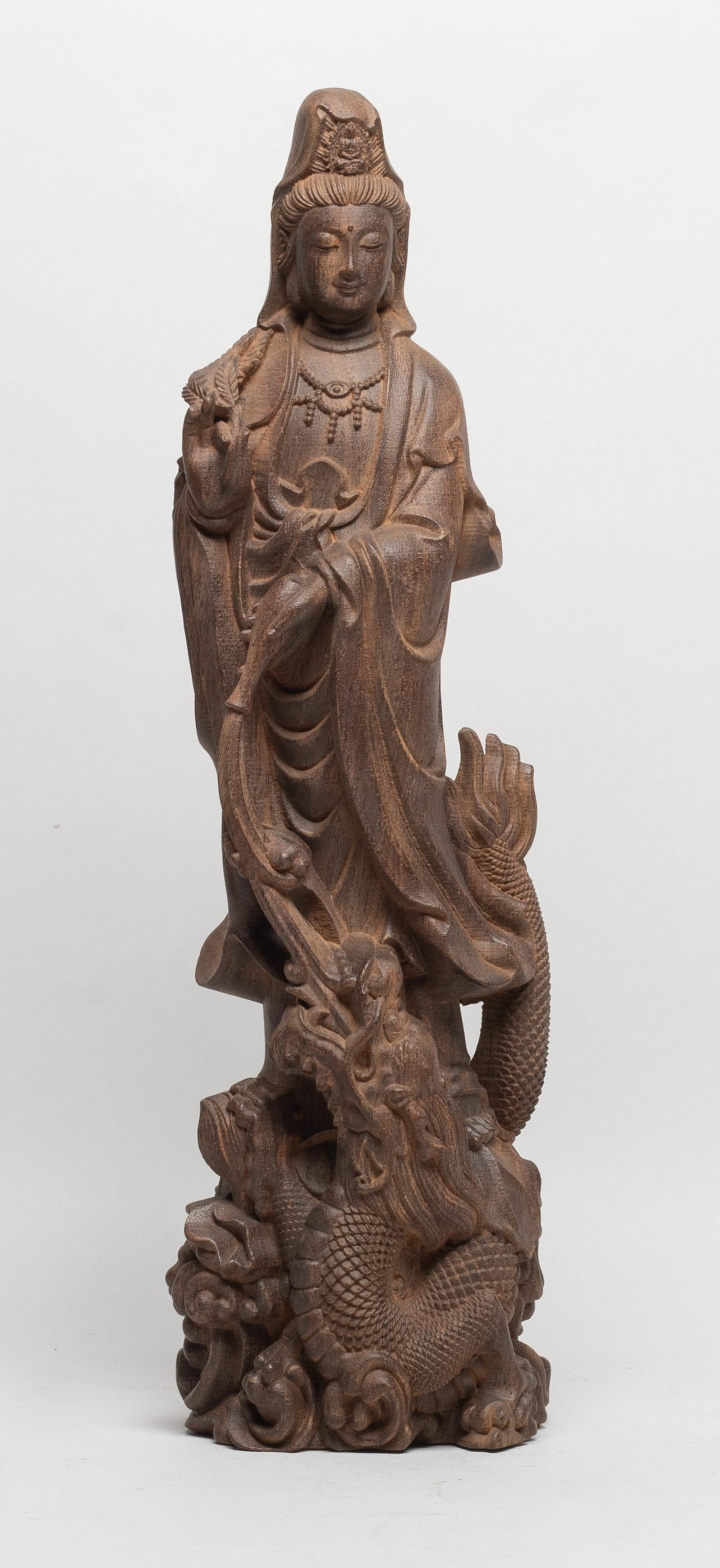 Tall Chinese Agarwood Carved Sculpture of Kuanyin: The Kuanyin carved standing on a sinuous dragon among waves, holding leaves in one hand and a bottle in the other hand spraying water into the dragon mouth, dressed in layered garments Approx.