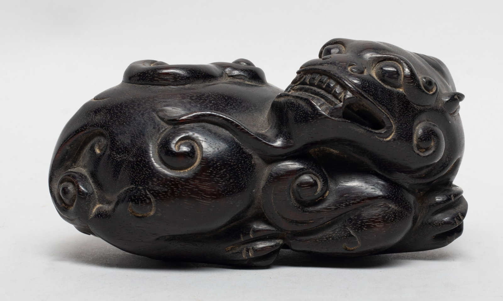 Chinese Zitan Wood Carved Sculpture: The wood beast carved in recumbent beast, its head turned sharply backward, detailed with bulging eyes and agape mouth revealing its teeth, the legs tucked under its body. Approx. 4.8*2.7*2.5 inch,