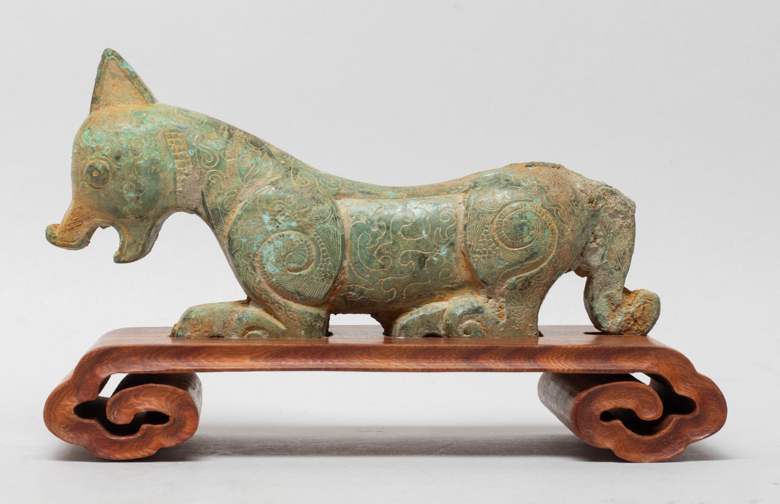 Estate Chinese Bronze Sculpture on Wood Base: Cast as a recumbent beast, the muscular body incised with archaistic scrolls, affixed to a wood base. Approx. 6.5*2.6*4 inch (w/ stand).