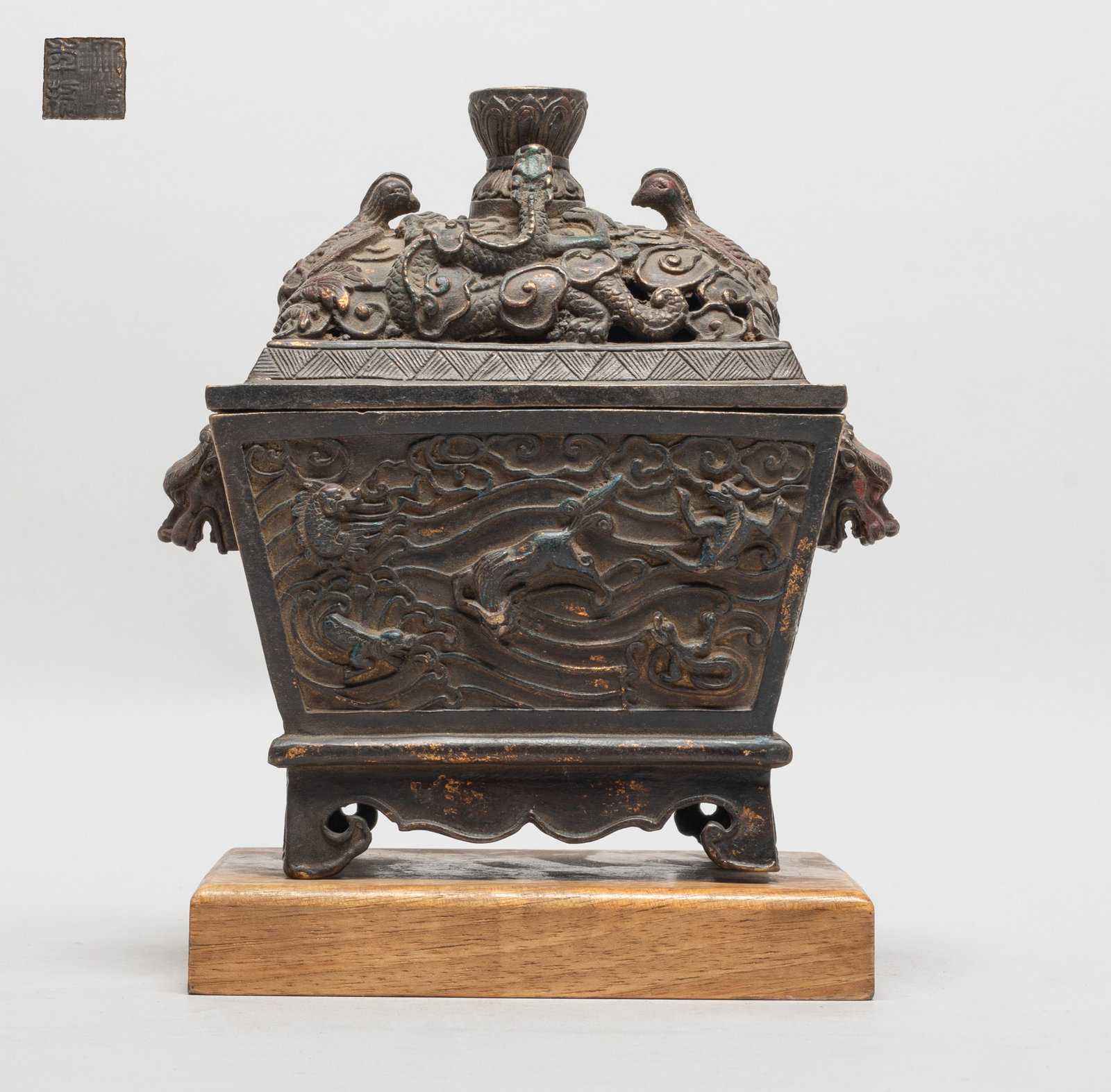 Chinese Bronze Covered Censer: Of tapered rectangular section with two raised mask handles, the sides cast with mythical beasts amidst clouds, the lid cast with dragon and phoenix amidst clouds, the bottom with a seal mark, with a