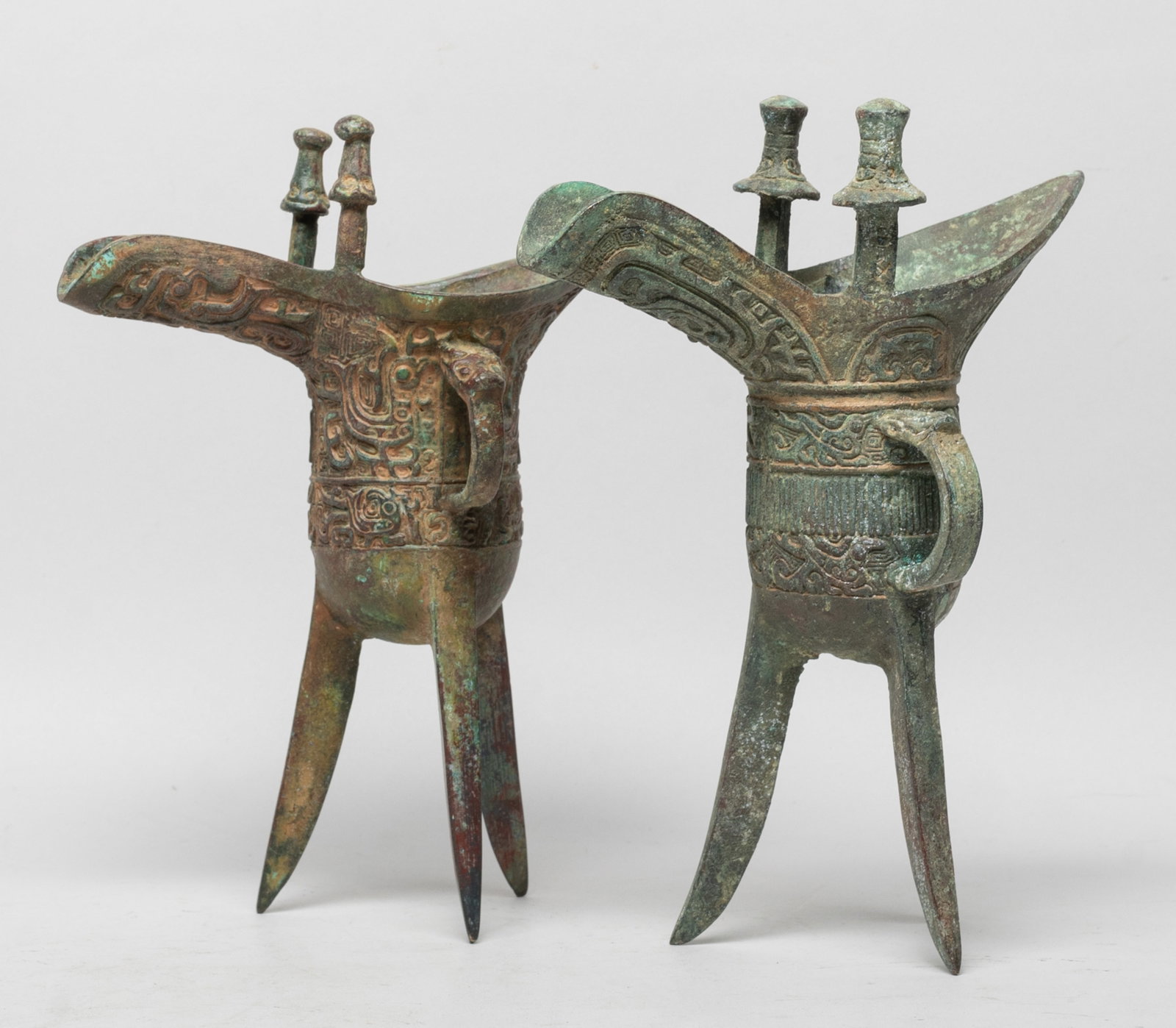 Two Chinese Bronze Tall Cups: Each bronze vessel cast with archaistic birds or beasts on leiwen ground, set with two capped finials, a handle and three legs. Approx. 7.7*5.7*3.1 inch (larger).