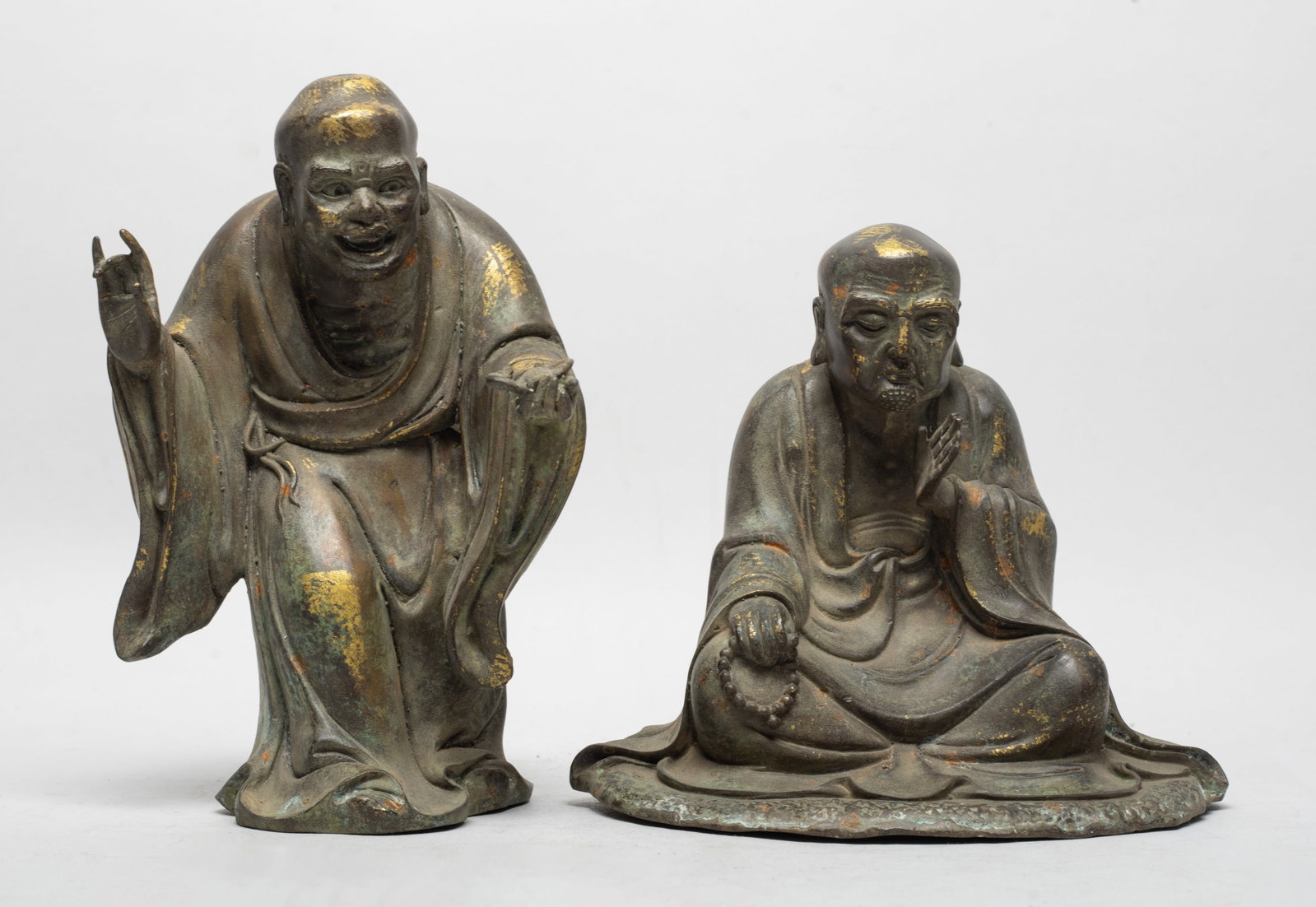 Two Chinese Bronze Sculptures of Luohan: Two bronze cast Luohan sculptures, dressed in low flowing robe, one standing and the other in seated pose. Approx. 7.3*4.6*4.3 inch (larger).