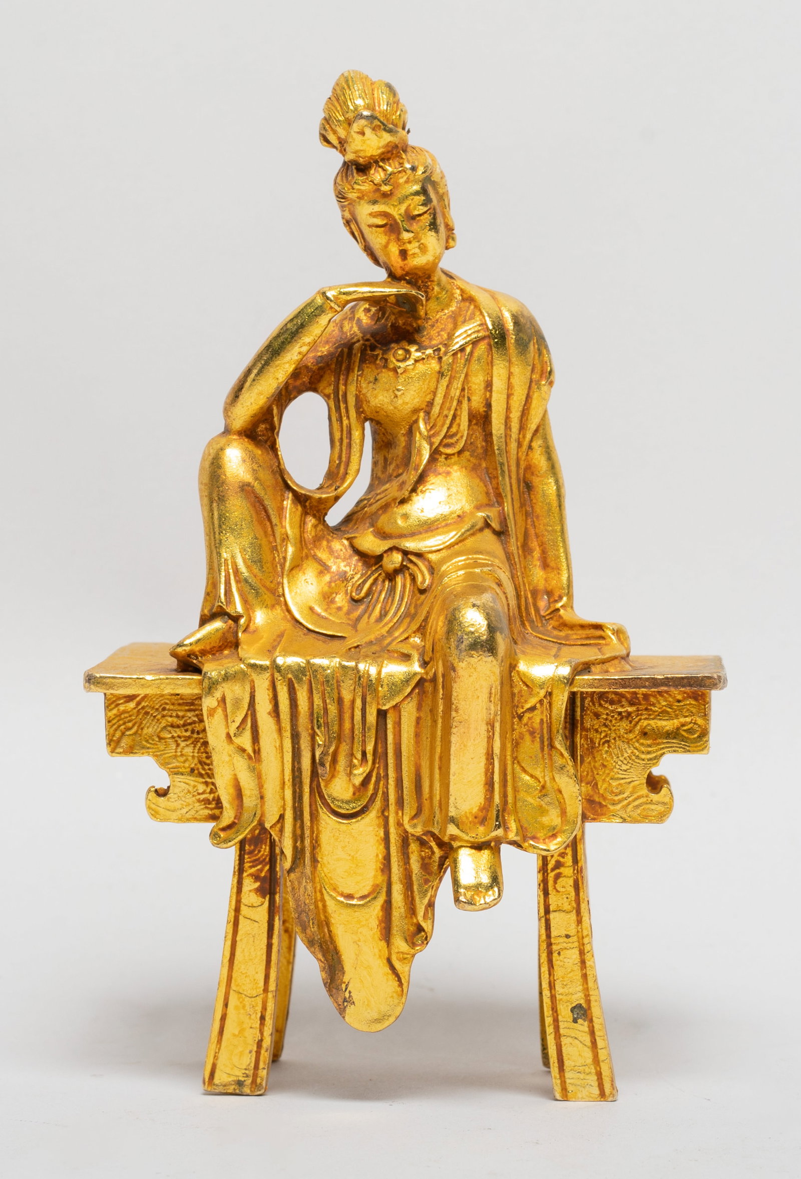 Rare Chinese Gold on Bronze Sculpture: The Buddha cast seated in a leisurely posture on a bench, wearing long curled scarf and loose-fitting dhoti, the face with serene expression. Approx. 5.2*3.2*2.2 inch.