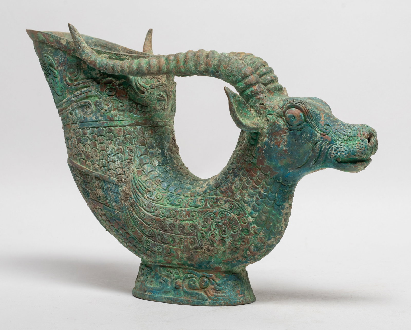 Estate Chinese Bronze Cup: Moulded of mythical beast form, the goat head with bulging eyes and long curled horns, the scaly body forming the cup cast with archaistic dragons. Approx. 10*6.9*3.5 inch.