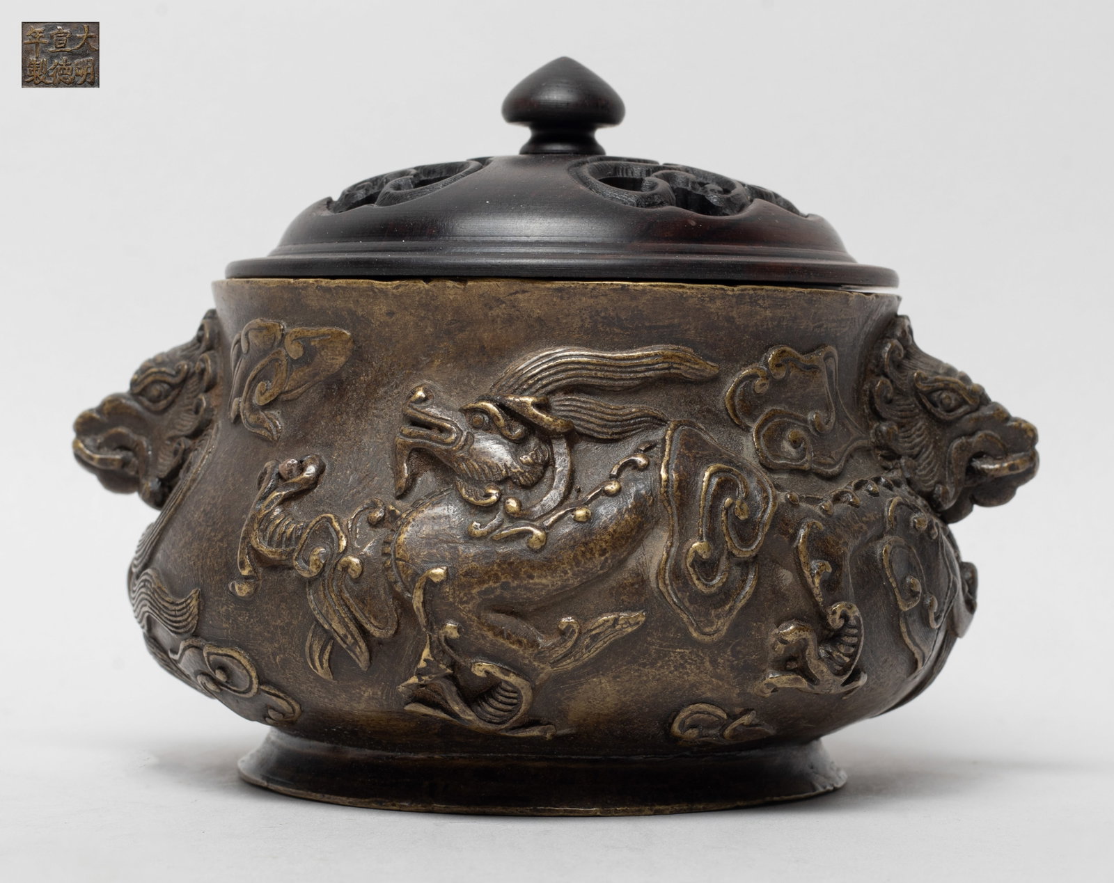 Chinese Bronze Censer w/ Wood Cover: The censer exterior cast in high relief with dragons sinuous amidst clouds, flanked by two raised masks, the bottom inscribed with a six-character mark, with an openwork wood cover. Approx. 5.4*4.6*2.