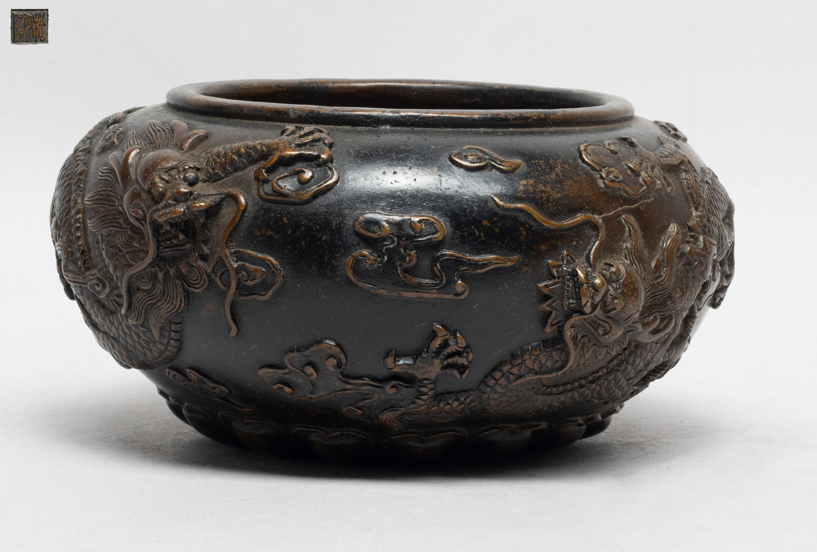 Estate Chinese Bronze Dragon Washer: Of compressed ovoid form, the washer exterior cast in raised relief with a pair of sinuous dragons amidst clouds above a band of petals, the bottom with a seal mark. Approx. 6.8*3.5 inch.