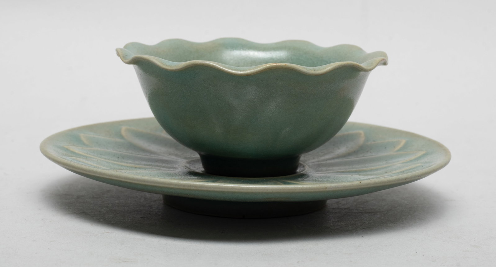 Chinese Longquan Type Porcleian Tea Cup: The tea cup rim molded of floral form, the saucer interior carved with a large flower, both covered with crackled celadon glaze. Approx. 5.5*2 inch (w/ saucer).