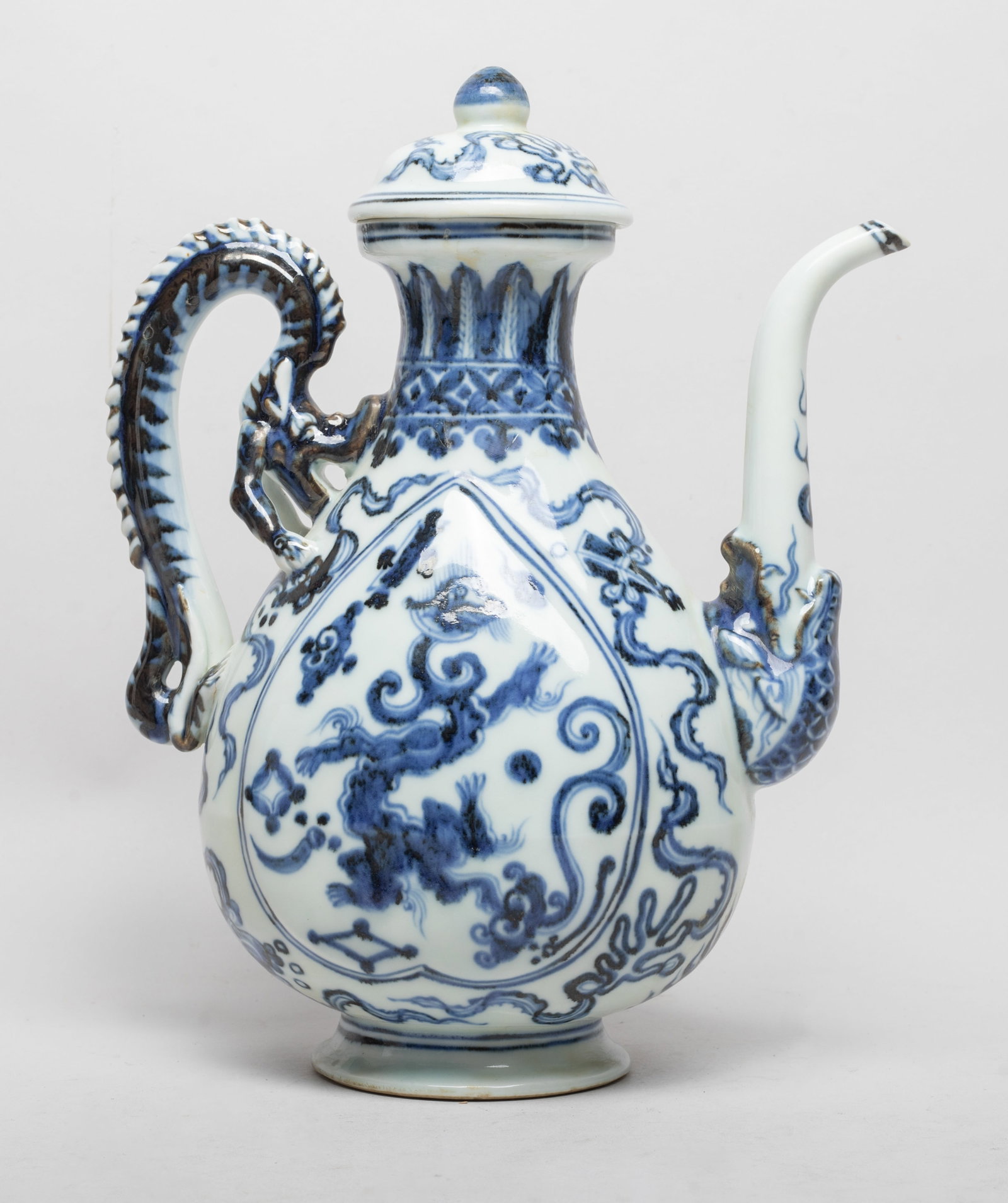 Large Chinese Export Porcelain Pot: The pear-shaped vase body with two peach-shaped panels enclosing dragons, surrounded by curled scarves, under a band of leaves, flanked with a dragon form handle and spout issuing from a dragon head.