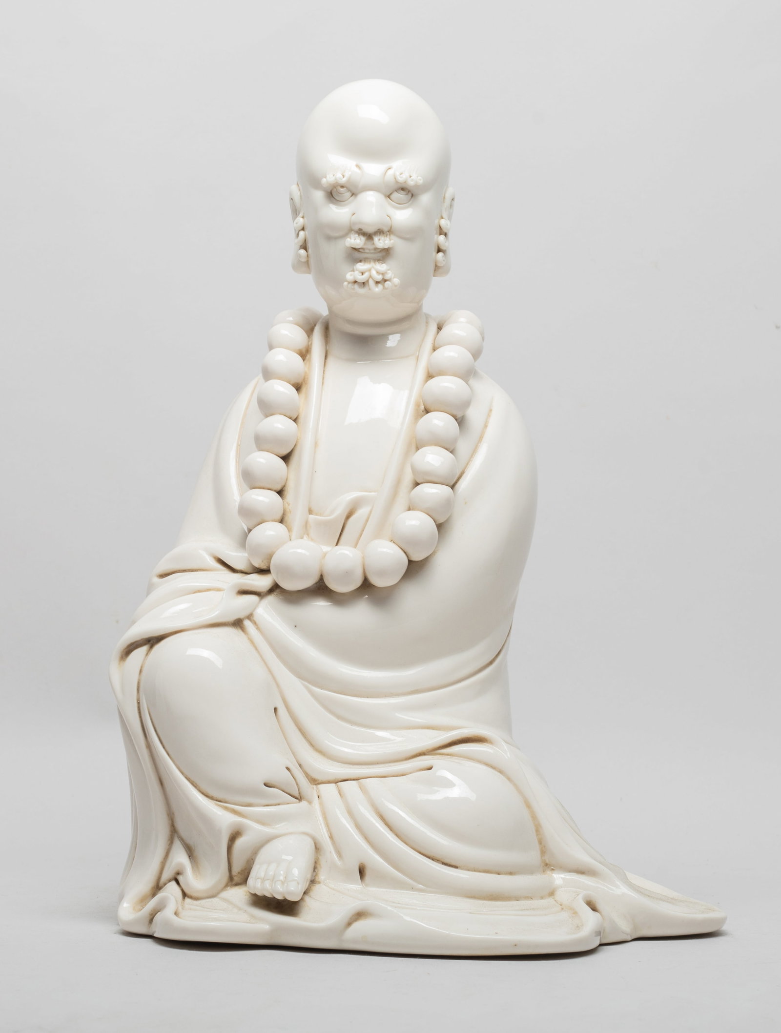 Estate Chinese Blank De Porcelain Sculpture: The hollow porcelain sculpture moulded as seated Buddha dressed in long flowing robe and large prayer beads, applied with creamy white glaze. Approx. 12.5*8.5*7.5 inch.