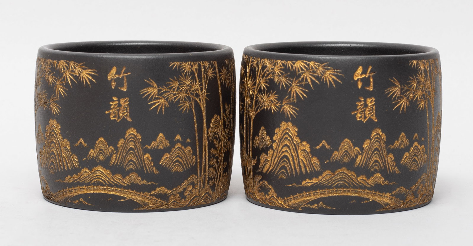 Two Chinese Gold Painted Zisha Tea Cups: Each cup exterior incised and painted in gold color with thick bamboo forest, a bridge and distant mountains, marked with two characters. Approx. 2.6*2 inch (each).
