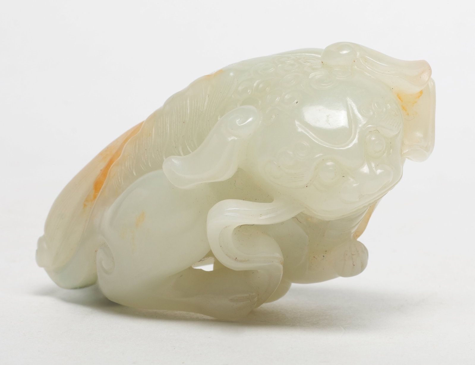 Chinese Russet Jade Carved Foo-Dog: Chinese almost-white and russet jade sculpture carved as a foo dog grasping a beribboned ball. Approx. 3.4*1.58*1.8 inch.